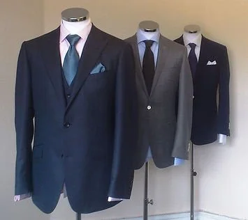 Three mannequins dressed in men's suits and ties displayed in a row