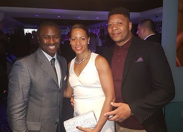 Three people dressed in formal attire at a social event, posing together and smiling for the camera.