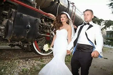 A bride and groom holding hands beside a vintage steam locomotive train.