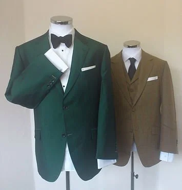 Two mannequins dressed in formal suits, one in a green tuxedo with a black bow tie and the other in a brown suit with a white shirt and brown tie.