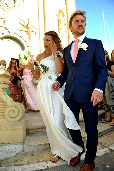 Bride and groom walking outside in front of a church, with bridesmaids and guests in the background.