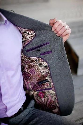 Person holding open gray blazer to reveal paisley and floral patterned lining with purple and pink accents.