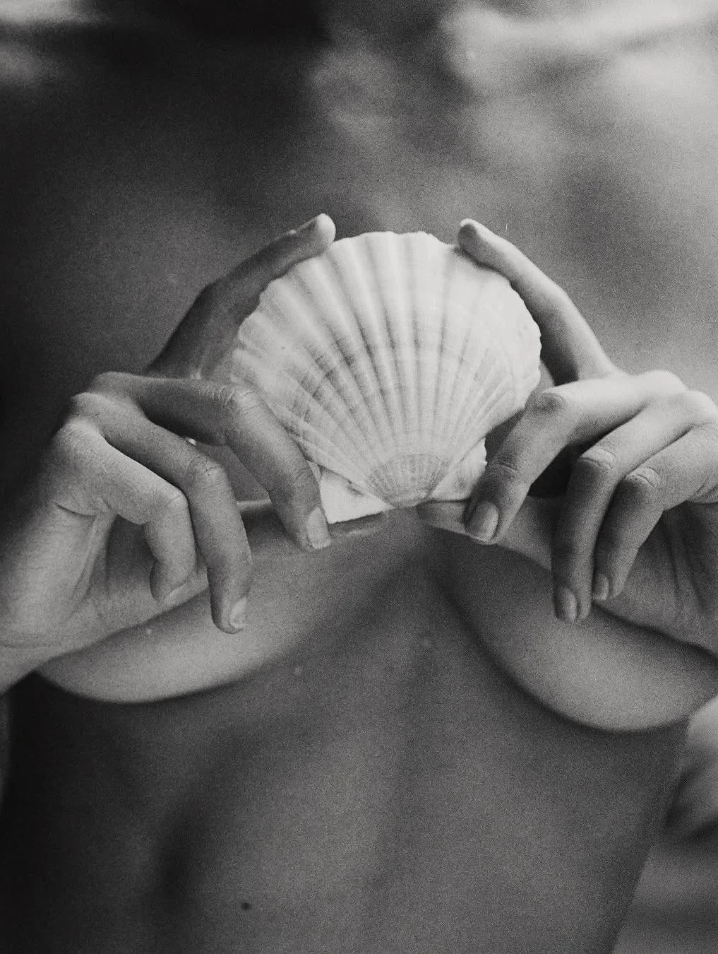 Black and white photo of two hands holding a seashell in front of the chest, with a cloudy sky in the background.
