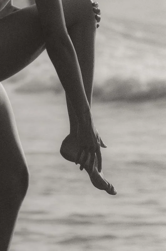 Close-up of a person's arm and hand hanging down over a body of water, black and white photograph.
