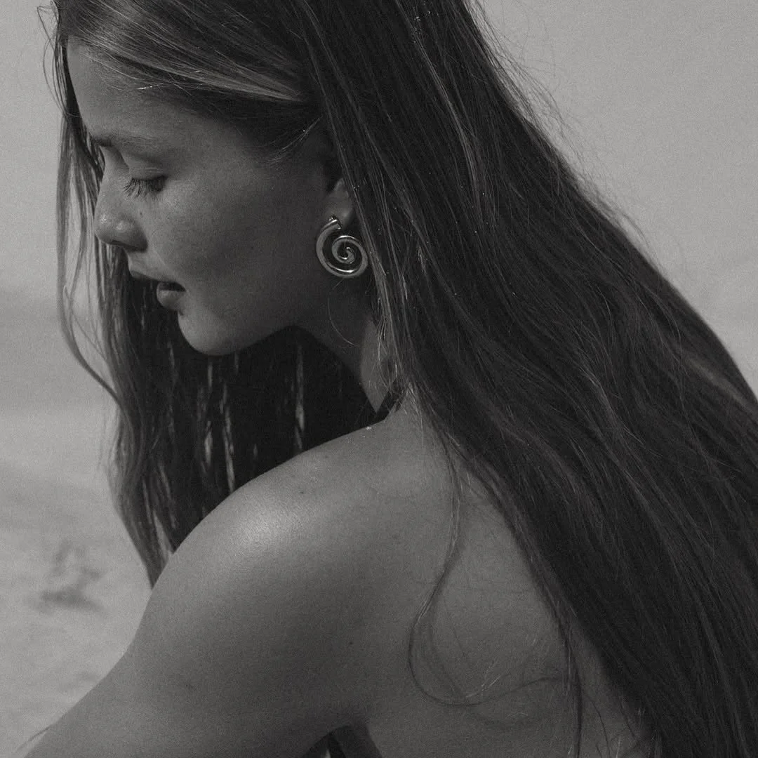 Black and white photo of a woman with long hair, earrings, and closed eyes, looking down.