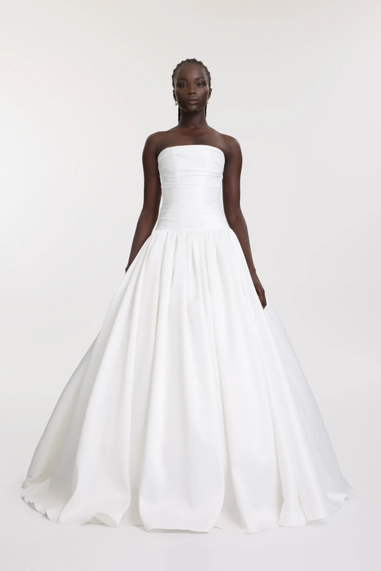 A woman in a strapless white wedding gown with a fitted bodice and full skirt standing against a plain light background.