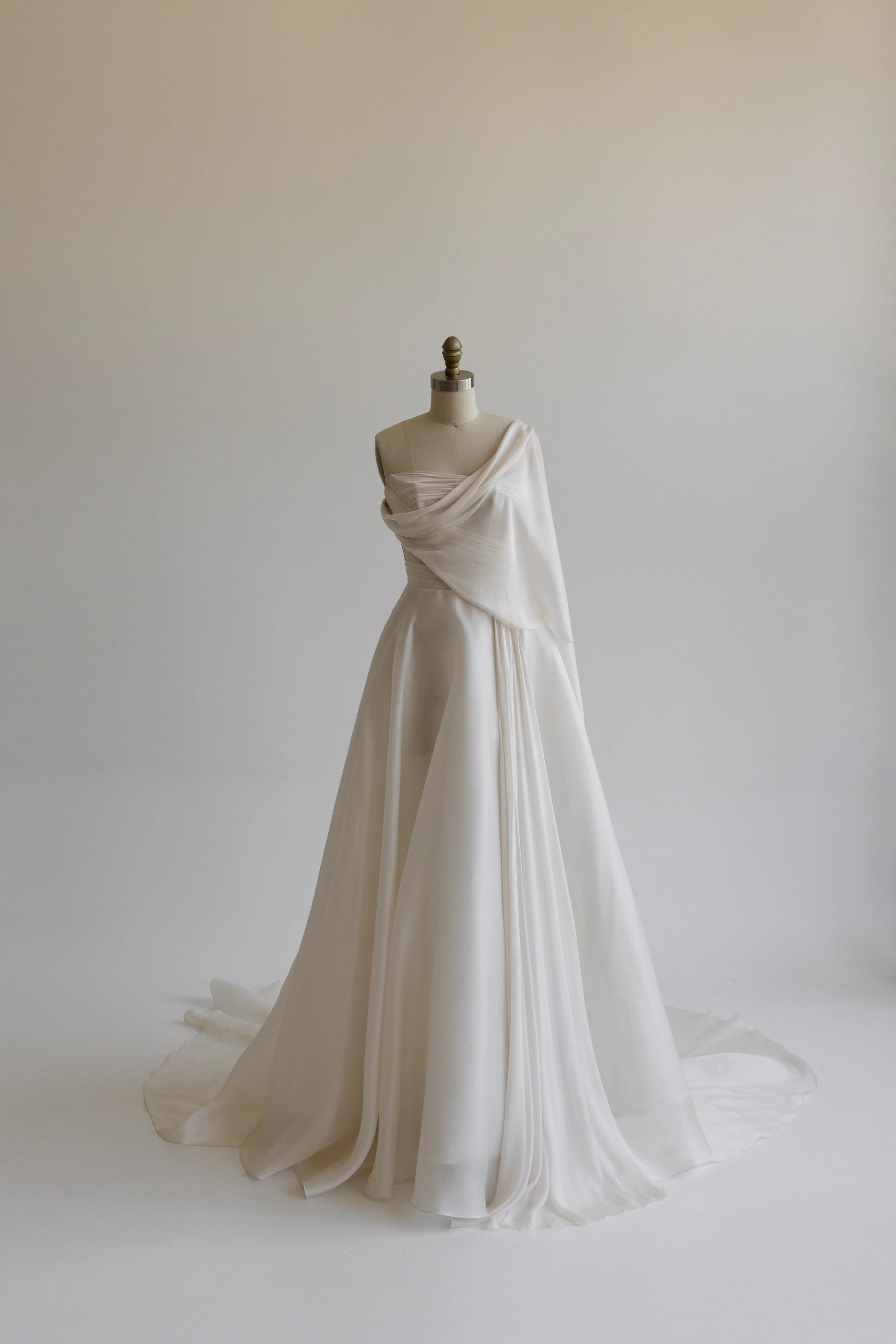 Elegant white wedding dress on a mannequin display with draped fabric design.