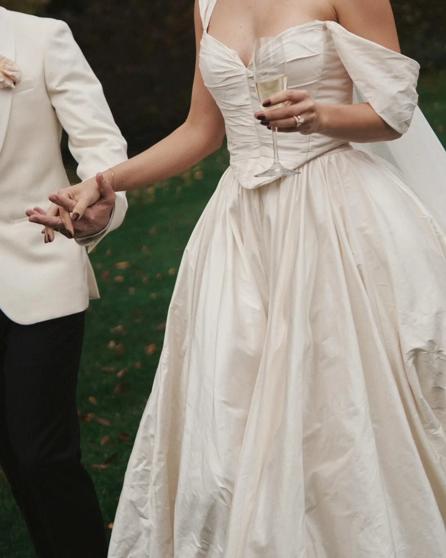 People dressed in formal wedding attire holding hands with one person holding a glass of champagne.