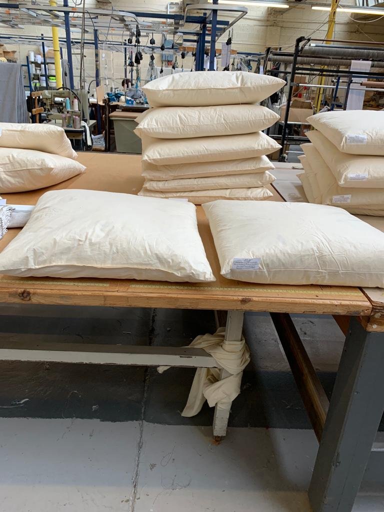 Stacked white pillows on a worktable in a factory or workshop setting.