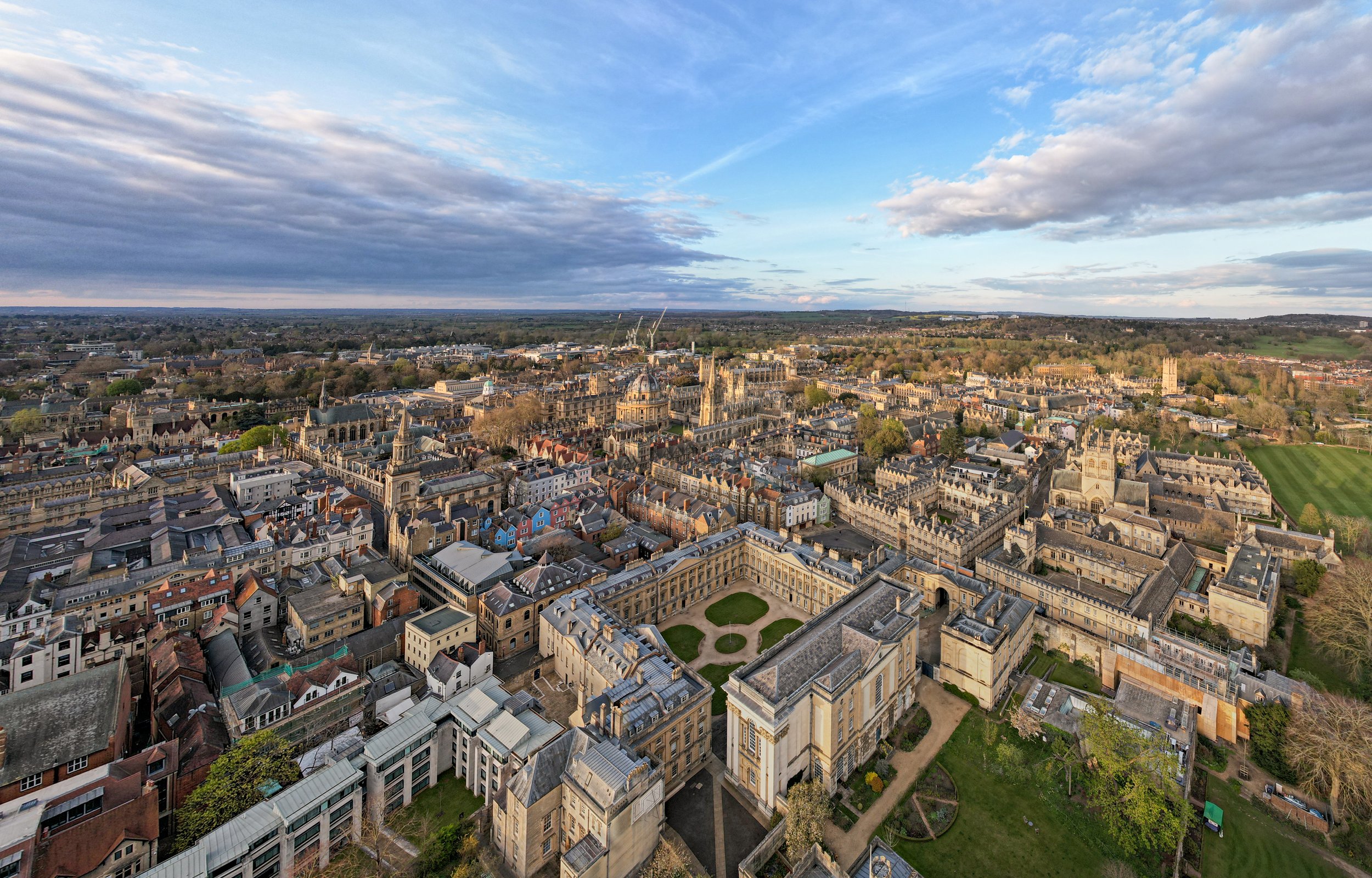 Aerial view of a historic city with churches, old buildings, and a central courtyard, under a partly cloudy sky.