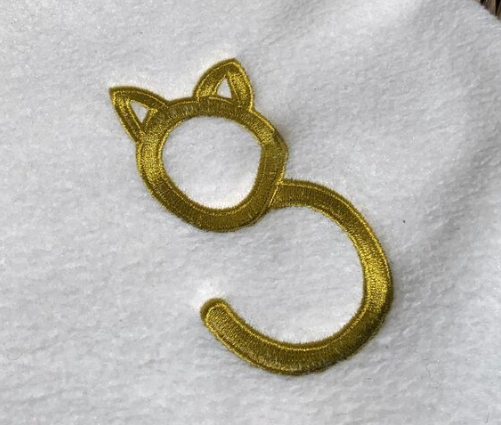 Gold embroidered hook shaped like a cat's head with ears, on white fabric.