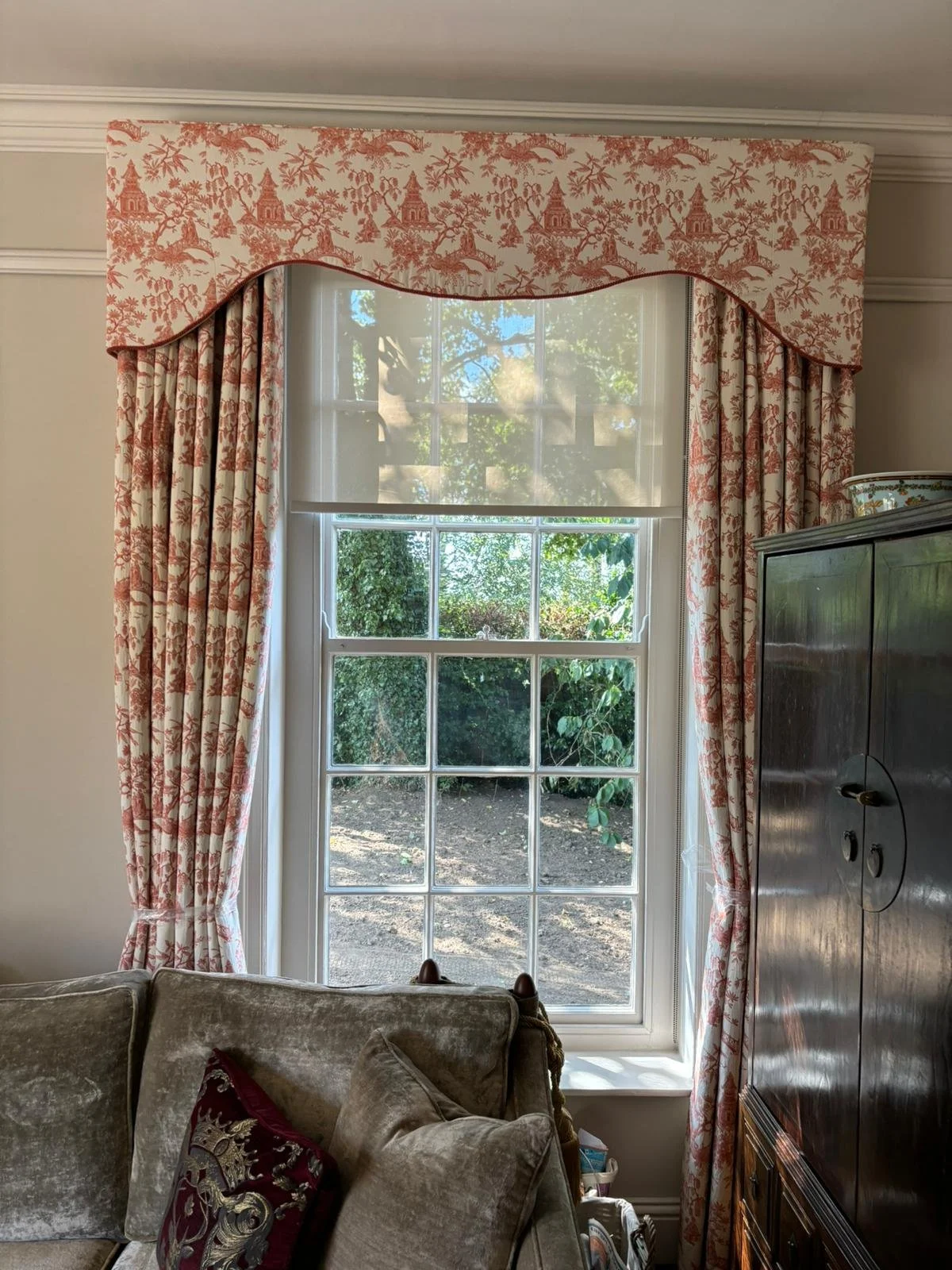 A window with patterned curtains and a valance, showing greenery outside, in a well-lit room.