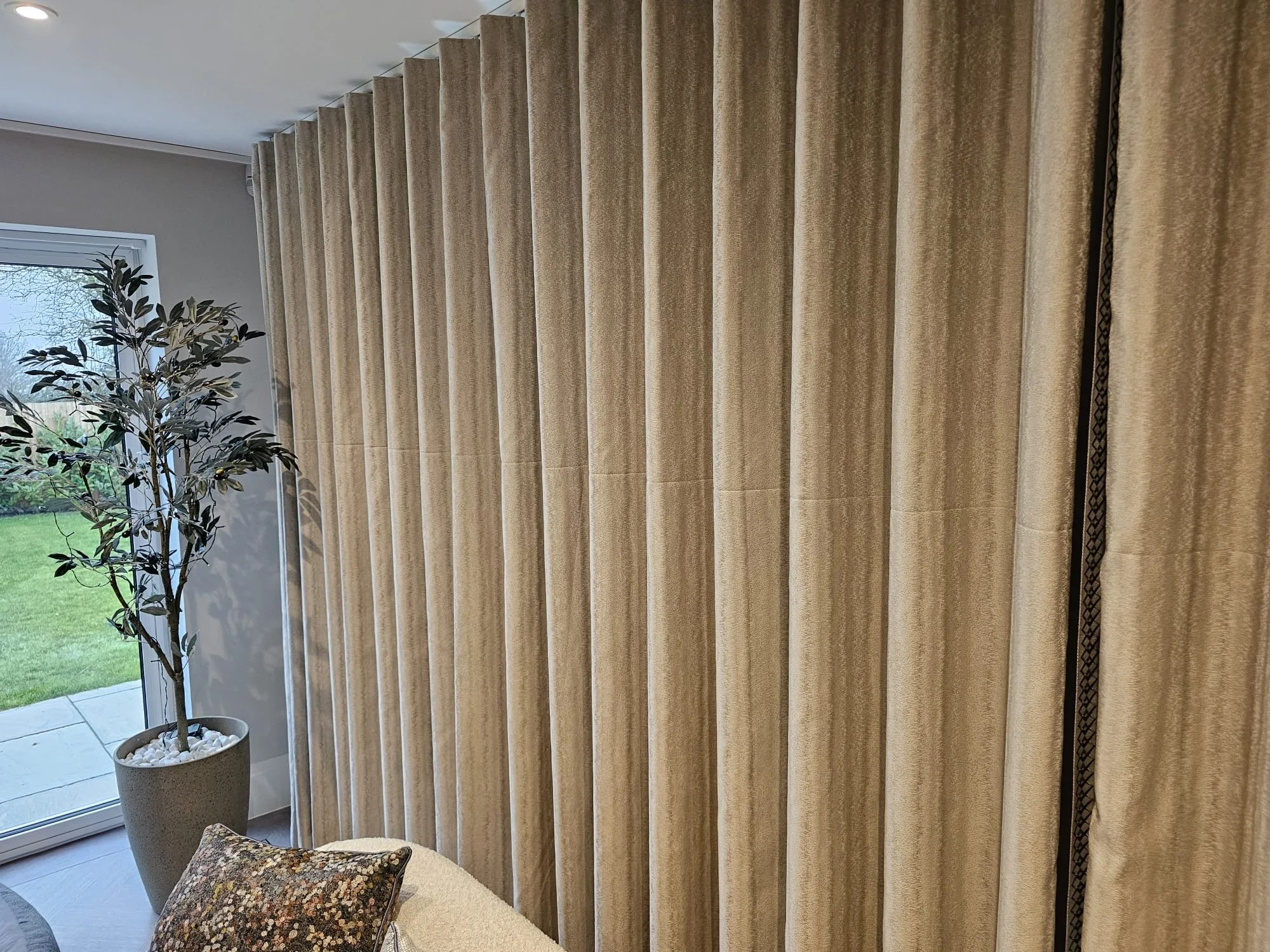 Interior living space with beige curtains covering large window and an indoor potted plant near the window.
