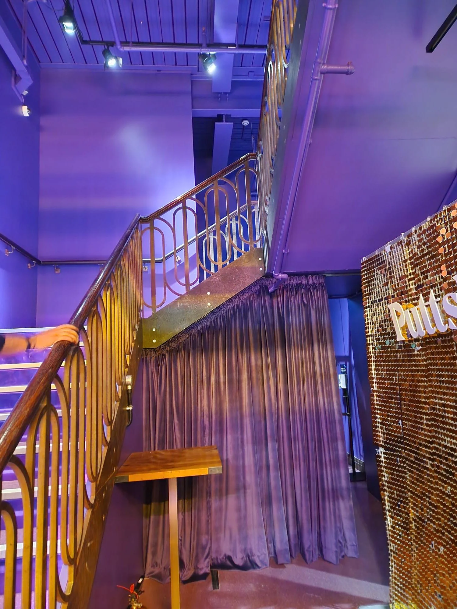 Interior of a building with a staircase, purple curtains, a gold-colored sign, and purple lighting.