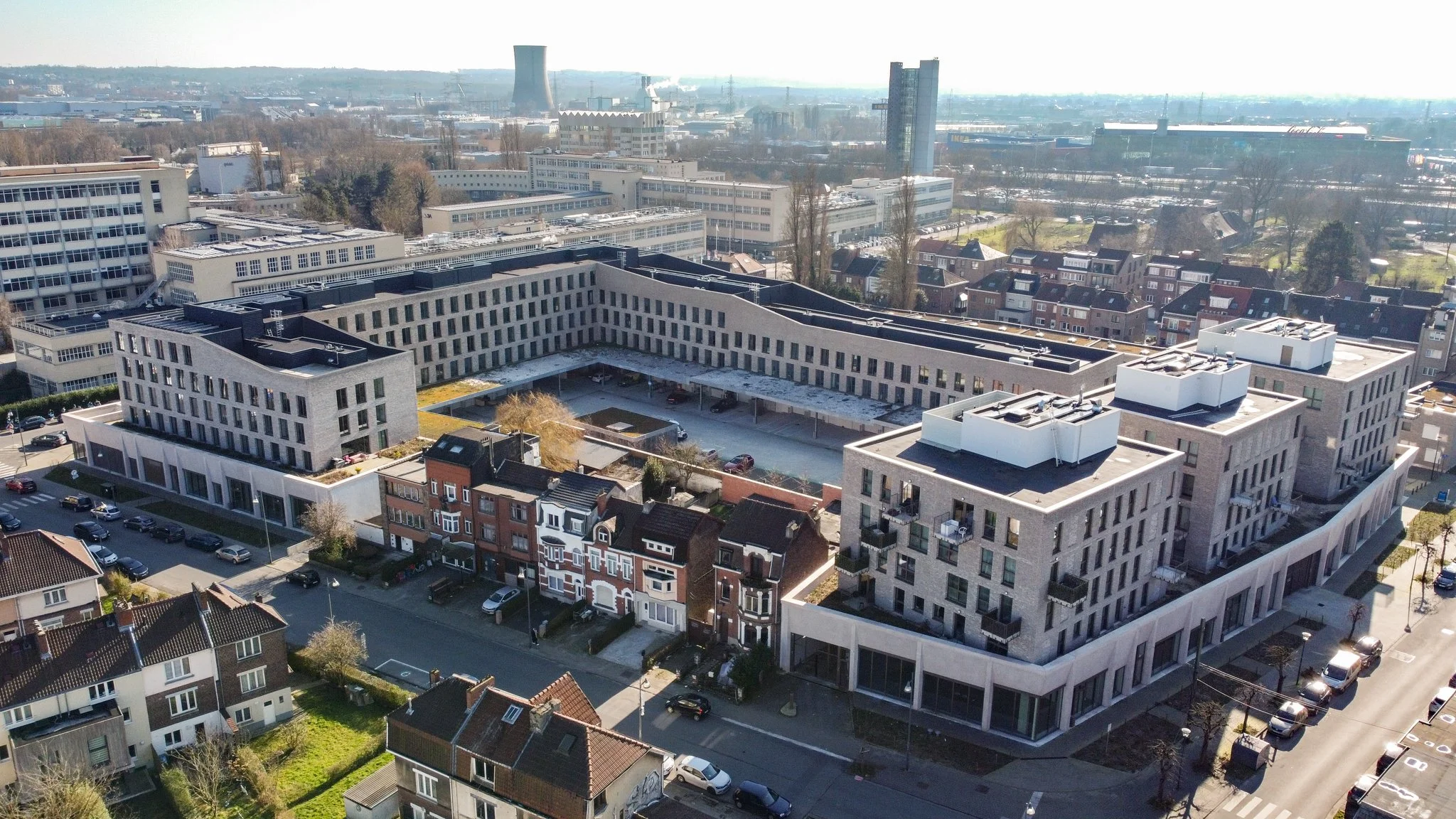Aerial view of a modern residential complex with a courtyard, surrounded by traditional houses and city buildings in the background.