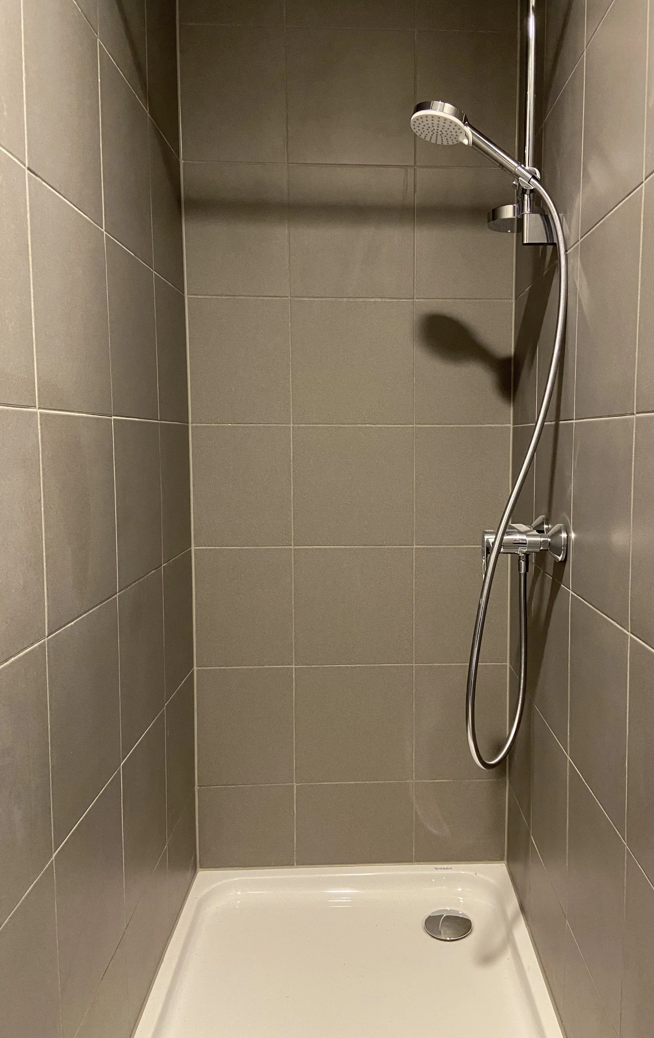 A shower area with tiled walls, a showerhead, and a drain on the floor.