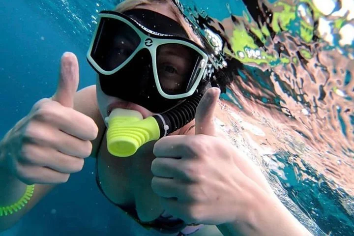 Person underwater wearing a black snorkel mask and giving two thumbs up