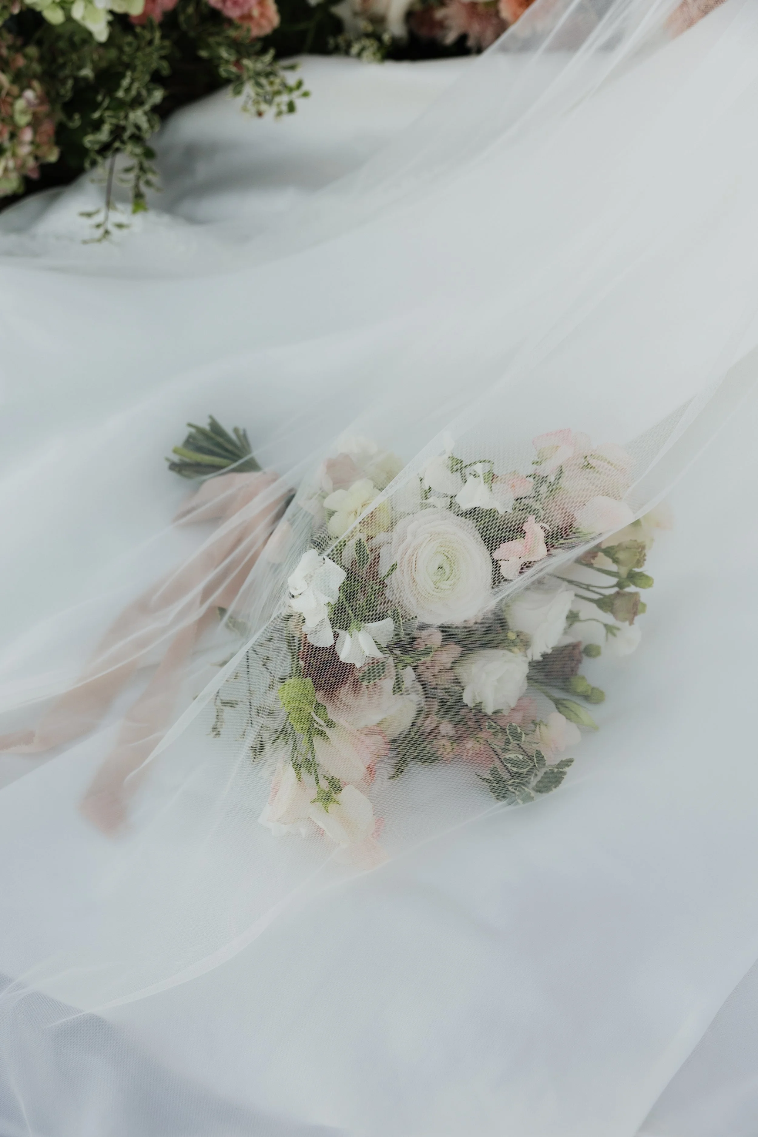 A bouquet of white, pink, and green flowers wrapped in a sheer white fabric, resting on a white surface.