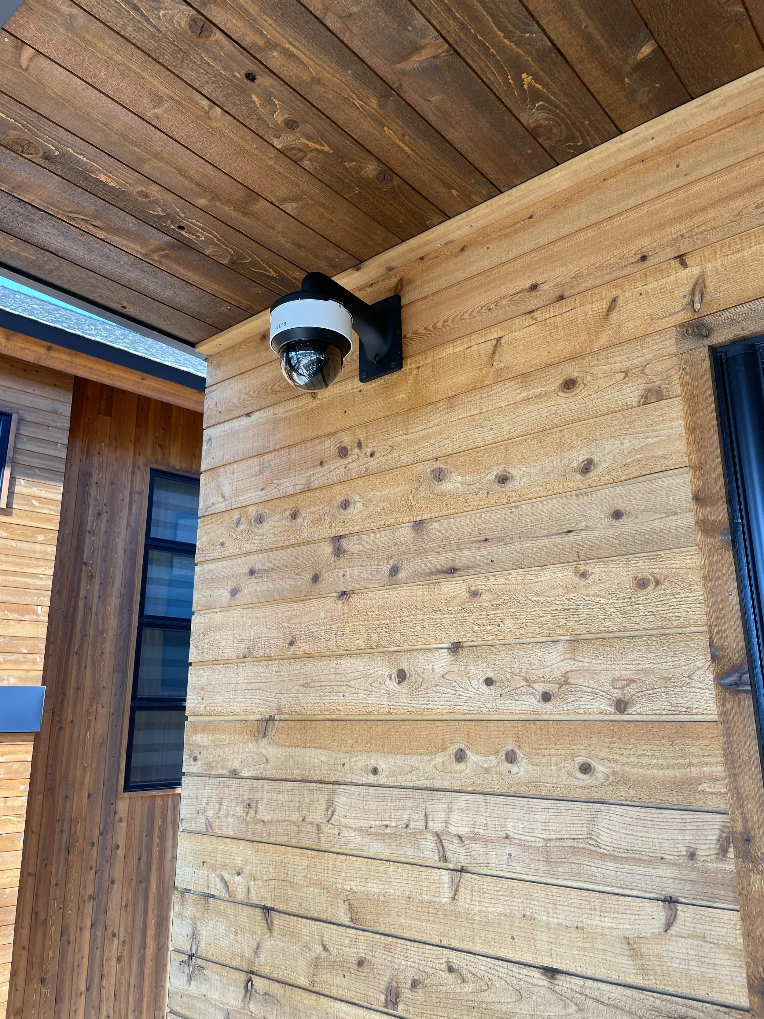 Security camera mounted on a wooden exterior wall of a building.