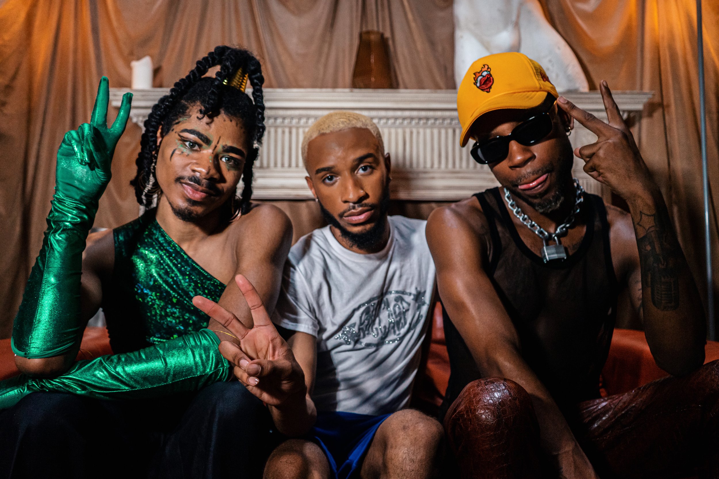 Three young men seated on a couch, making peace signs and playful gestures.