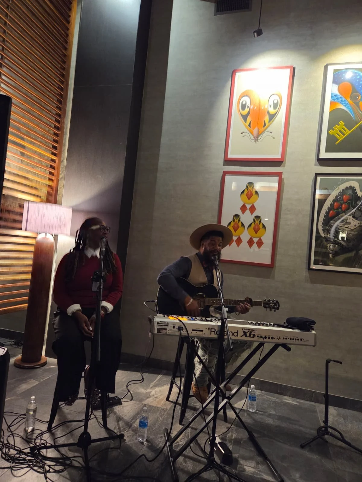 Musicians performing with a keyboard and guitar in an indoor venue with modern decor and artwork on the wall.