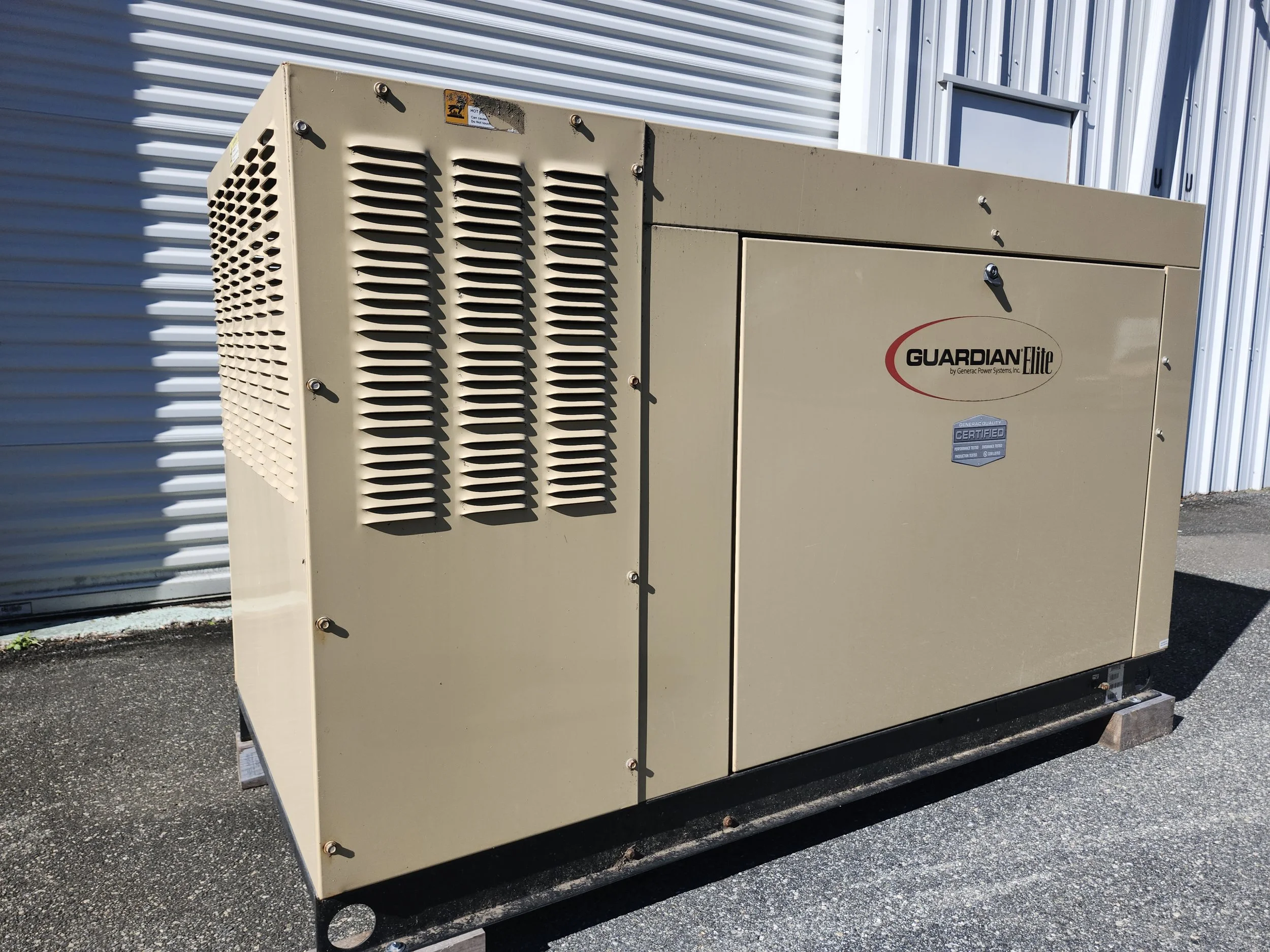 Industrial beige cooling or power equipment with vents, labeled Guardian Elite, placed on a metal stand outside near a metal building.