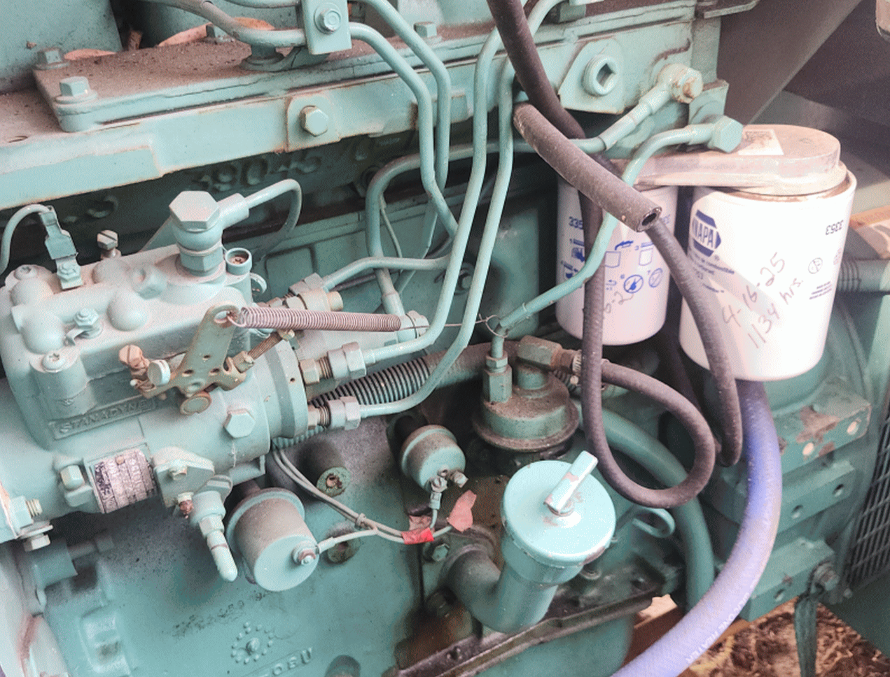 Close-up of a vintage industrial machine or engine with various pipes, filters, and components, painted in a light green color, some parts showing rust and wear.