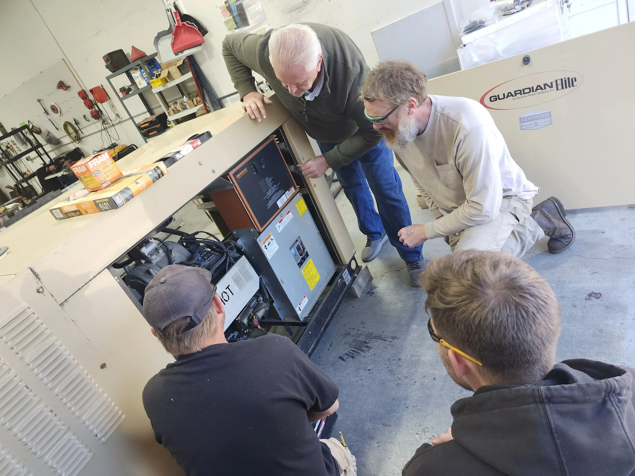 Group of four men working together in a workshop around a large piece of equipment, with tools and supplies in the background.