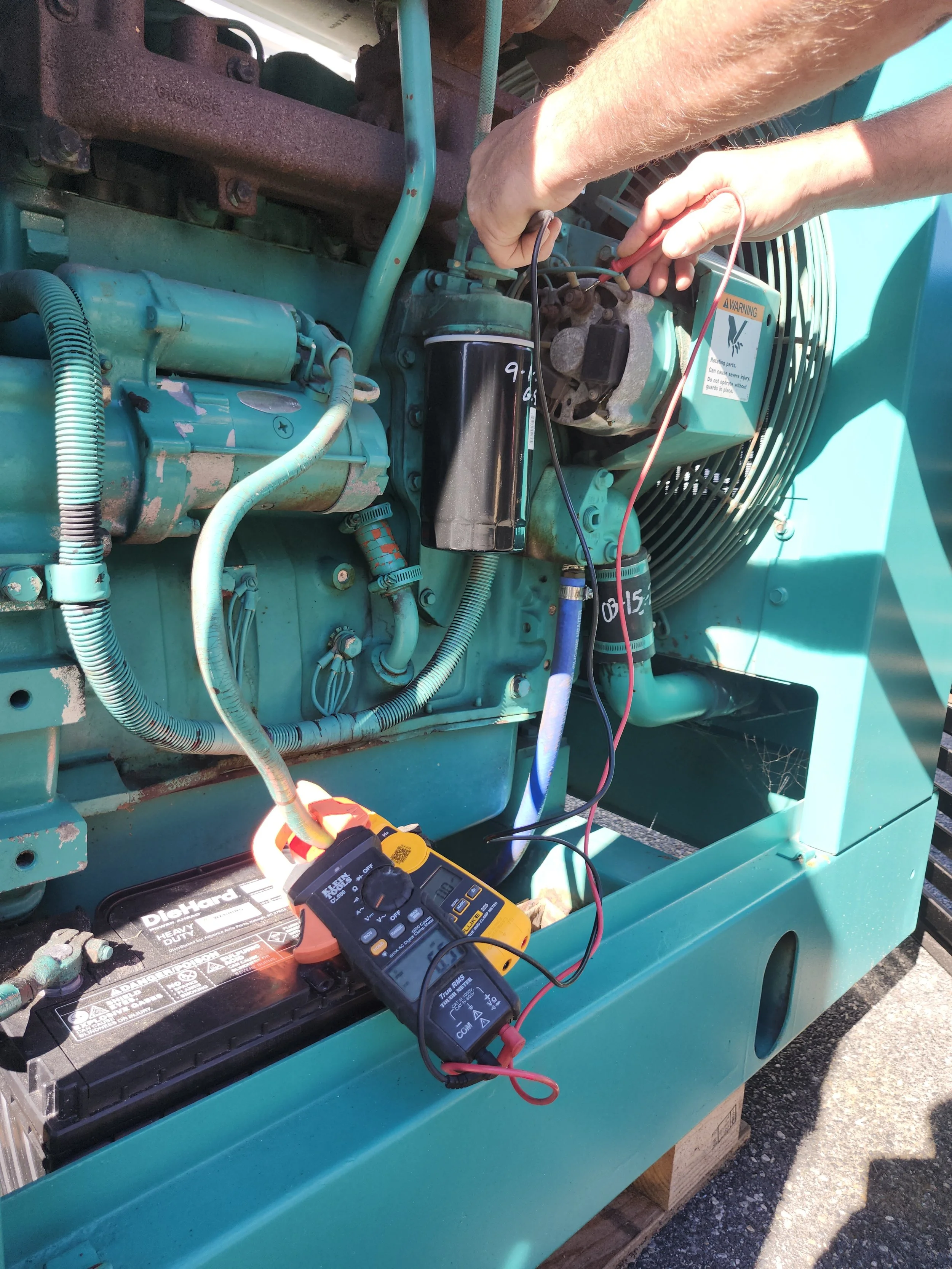 Technician using a multimeter to test electrical connections on a large teal-colored industrial generator.