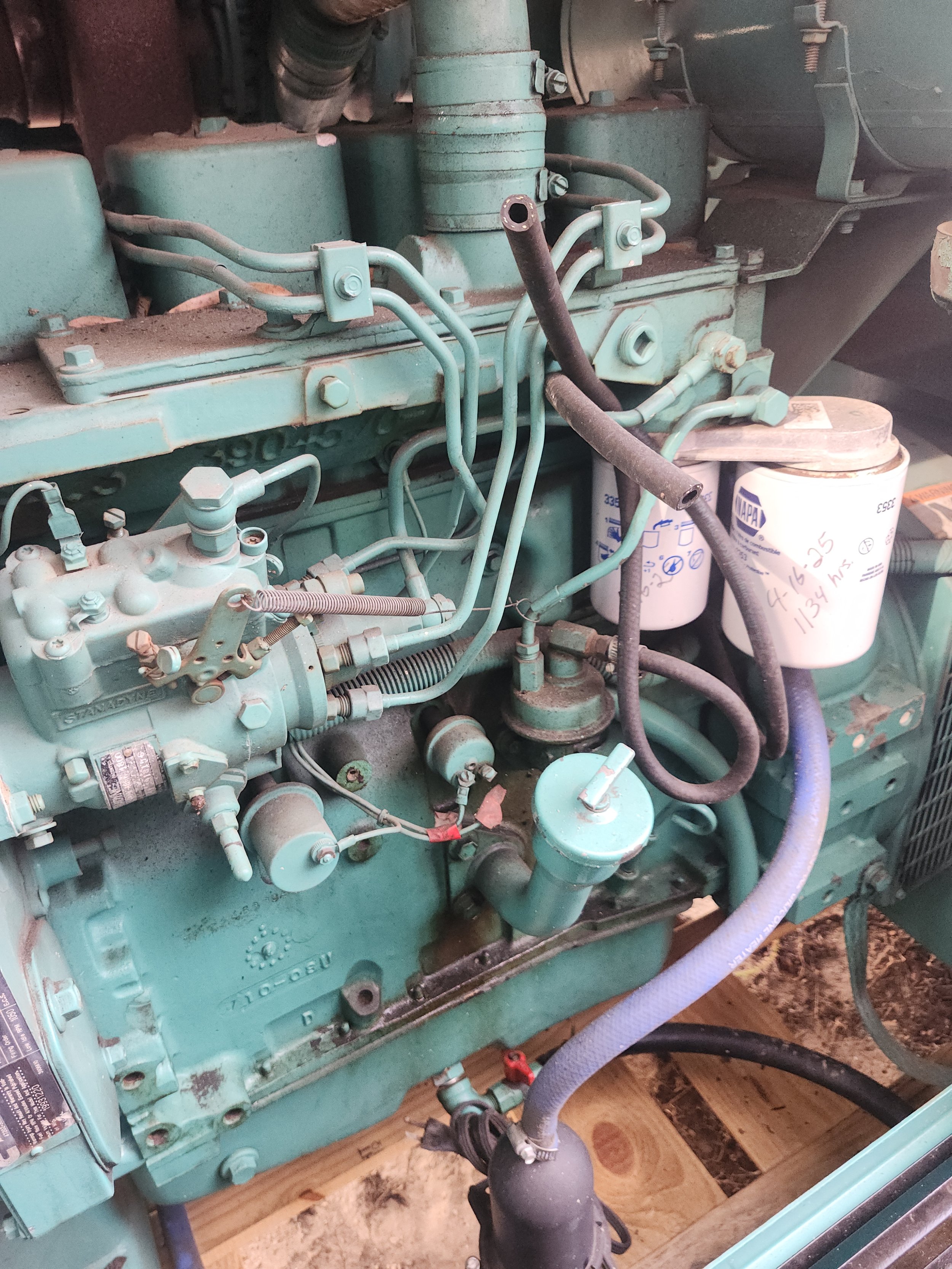 Close-up view of an industrial diesel engine with various pipes, hoses, and filters, mounted on a wooden platform.