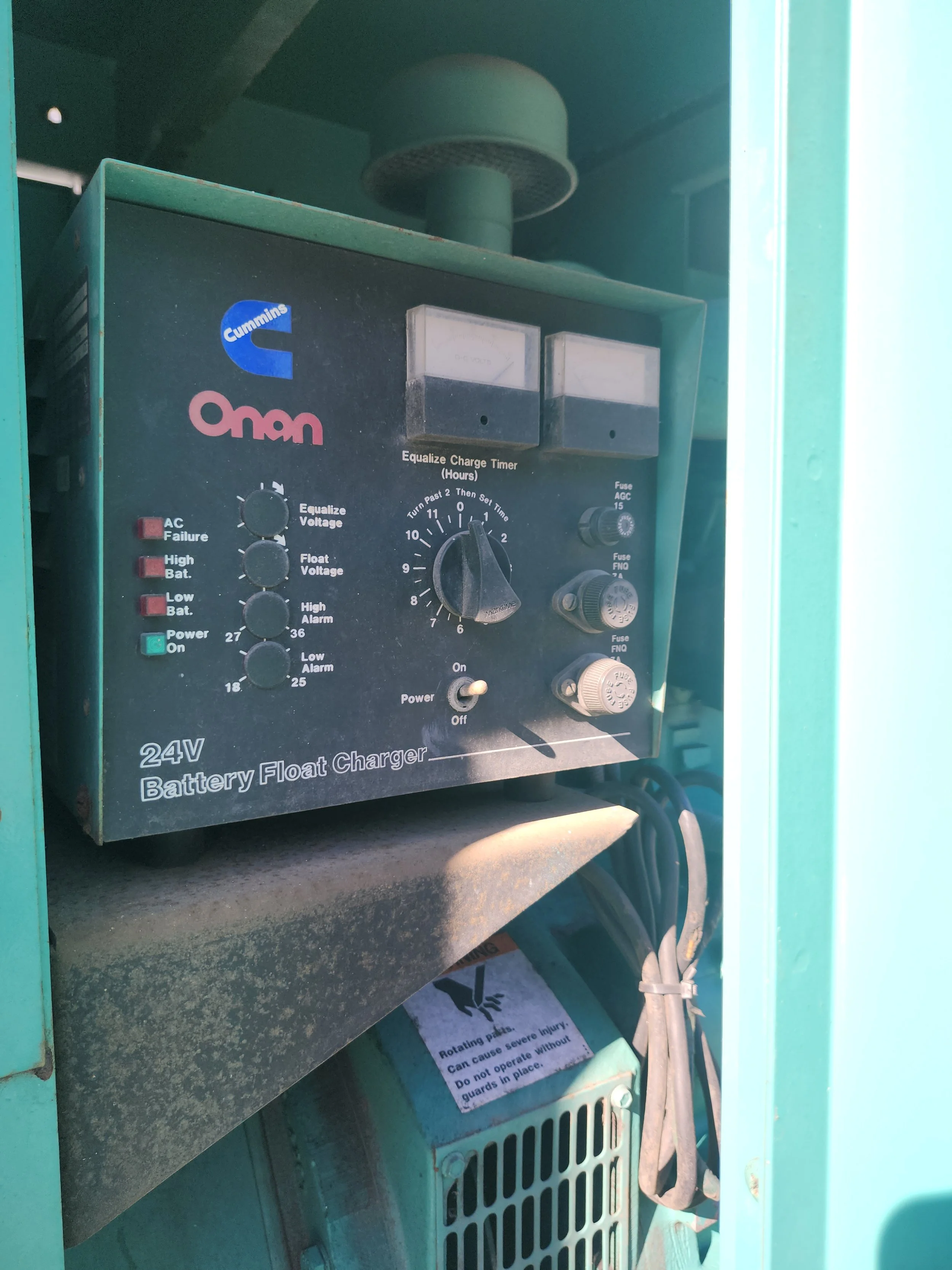 A 24-volt battery float charger with a black control panel featuring knobs, lights, and digital meters, mounted inside a green structure.