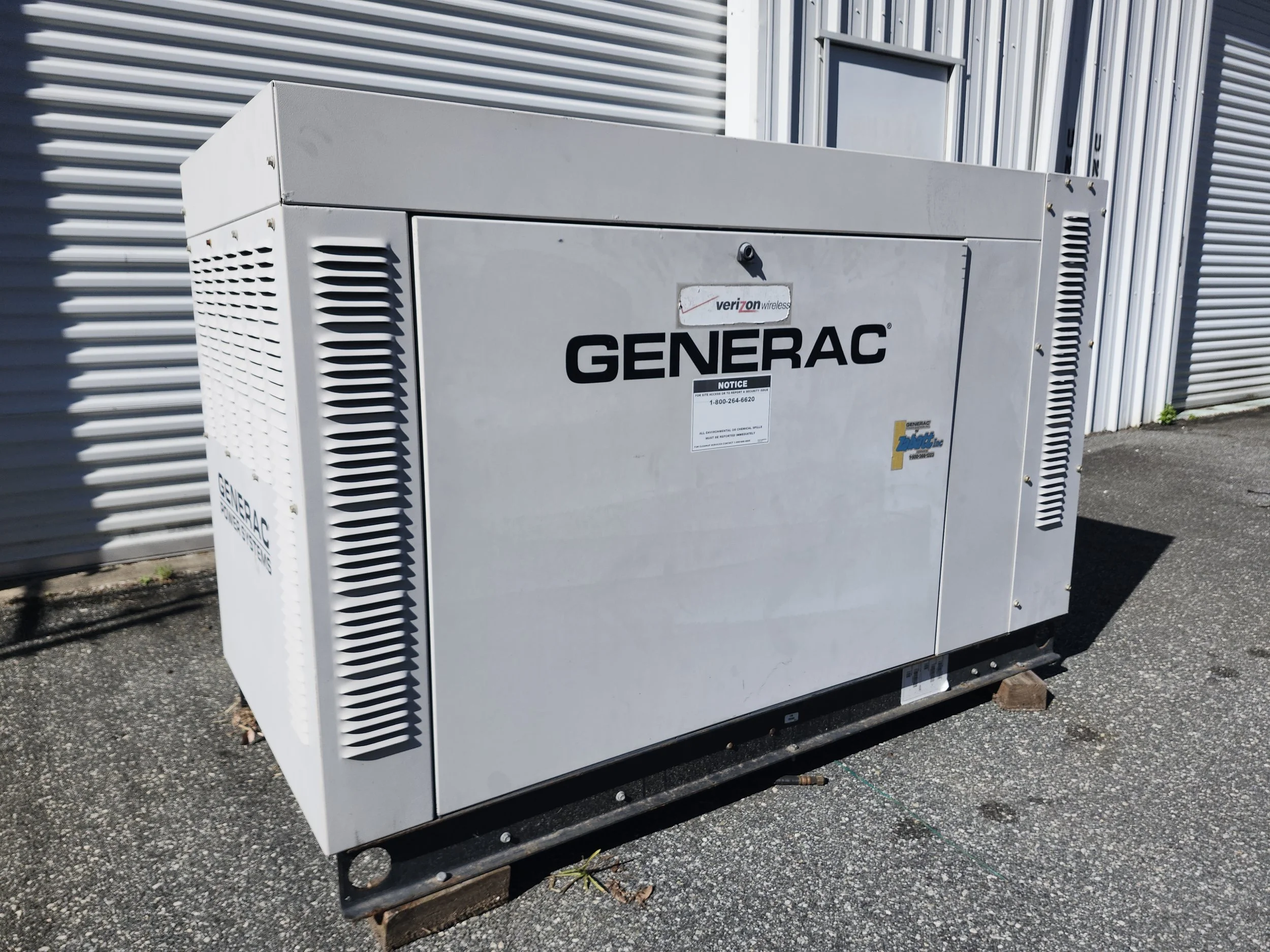 Outdoor industrial generator with Generac branding on a concrete surface near a metal-clad building.