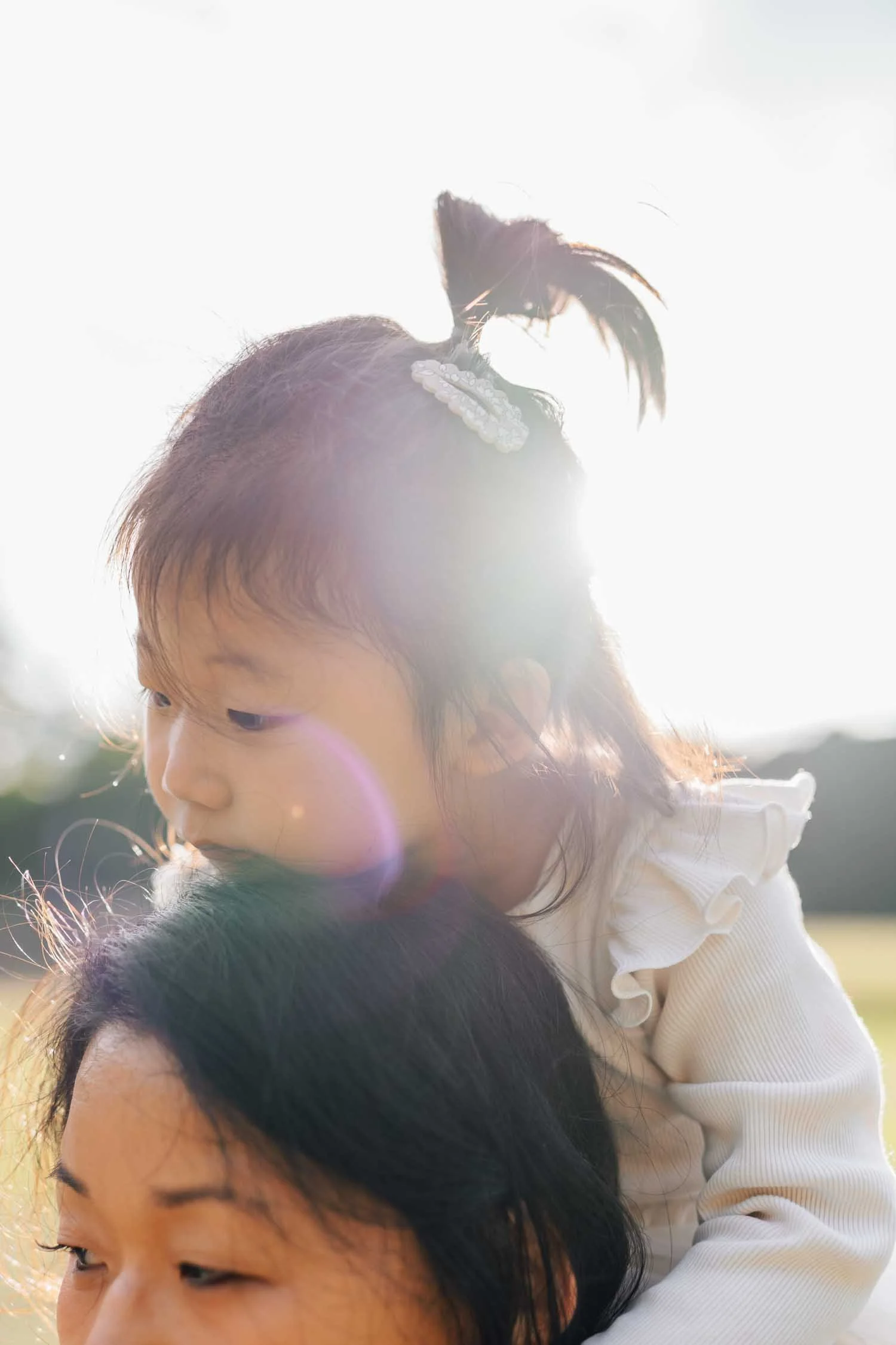 Close-up of a little girl sitting on her mother’s shoulders with soft, artistic light during a family photography session in Raleigh, North Carolina.