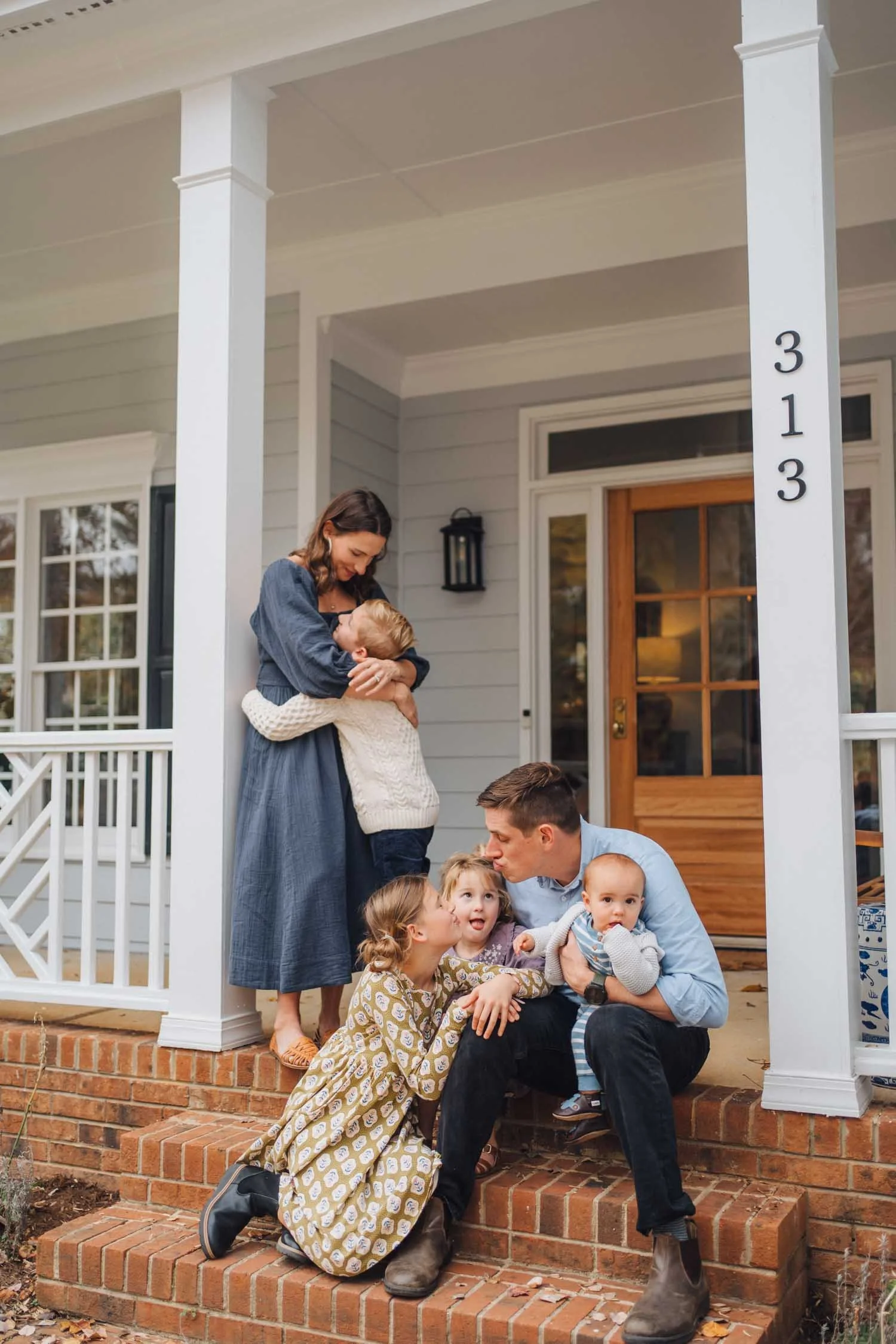 Two parents sitting on their front porch laughing with their children and baby during a relaxed family photography session in North Carolina.