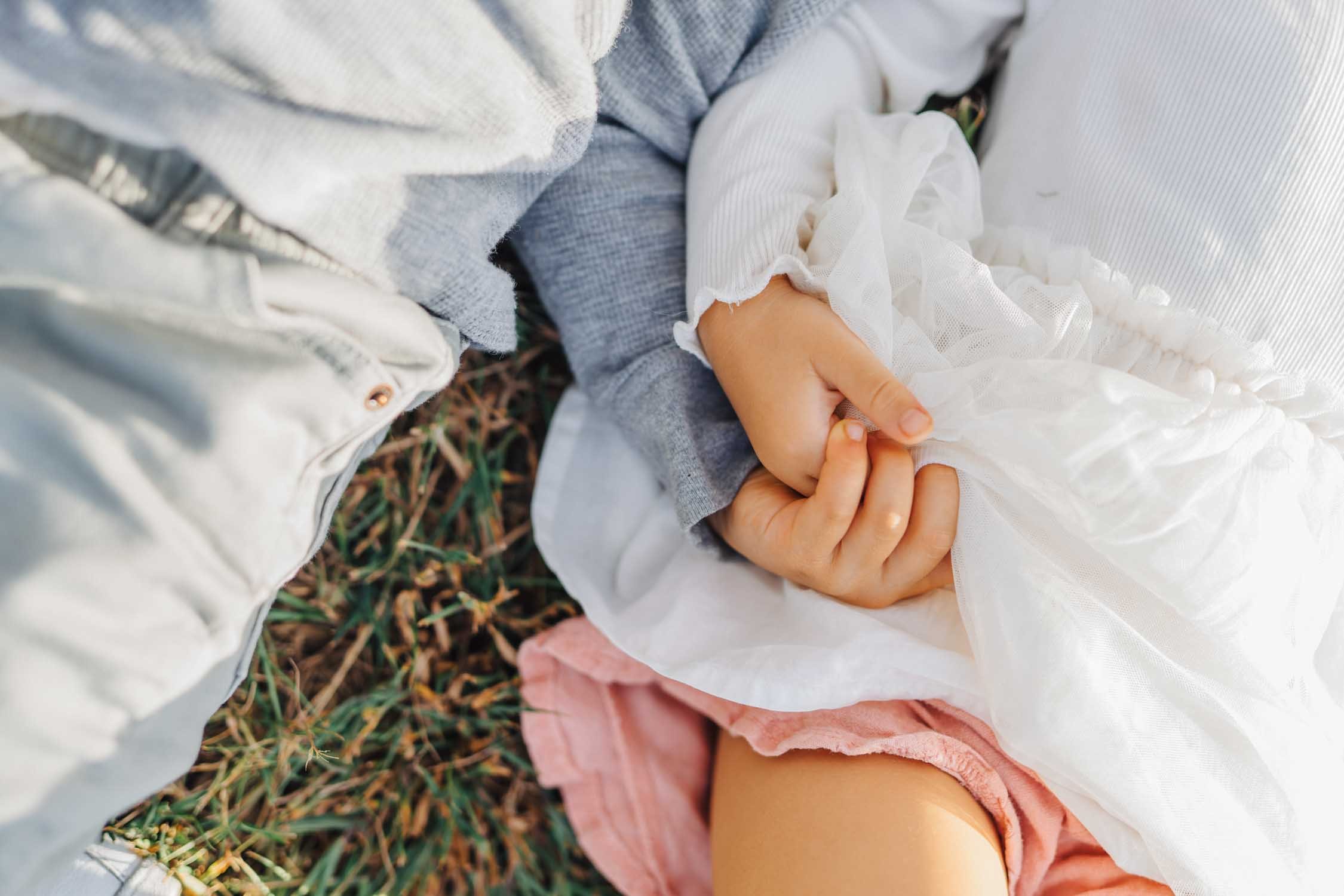 Close-up of two young siblings holding hands in the grass during a park family photography session by a Raleigh, NC family photographer.