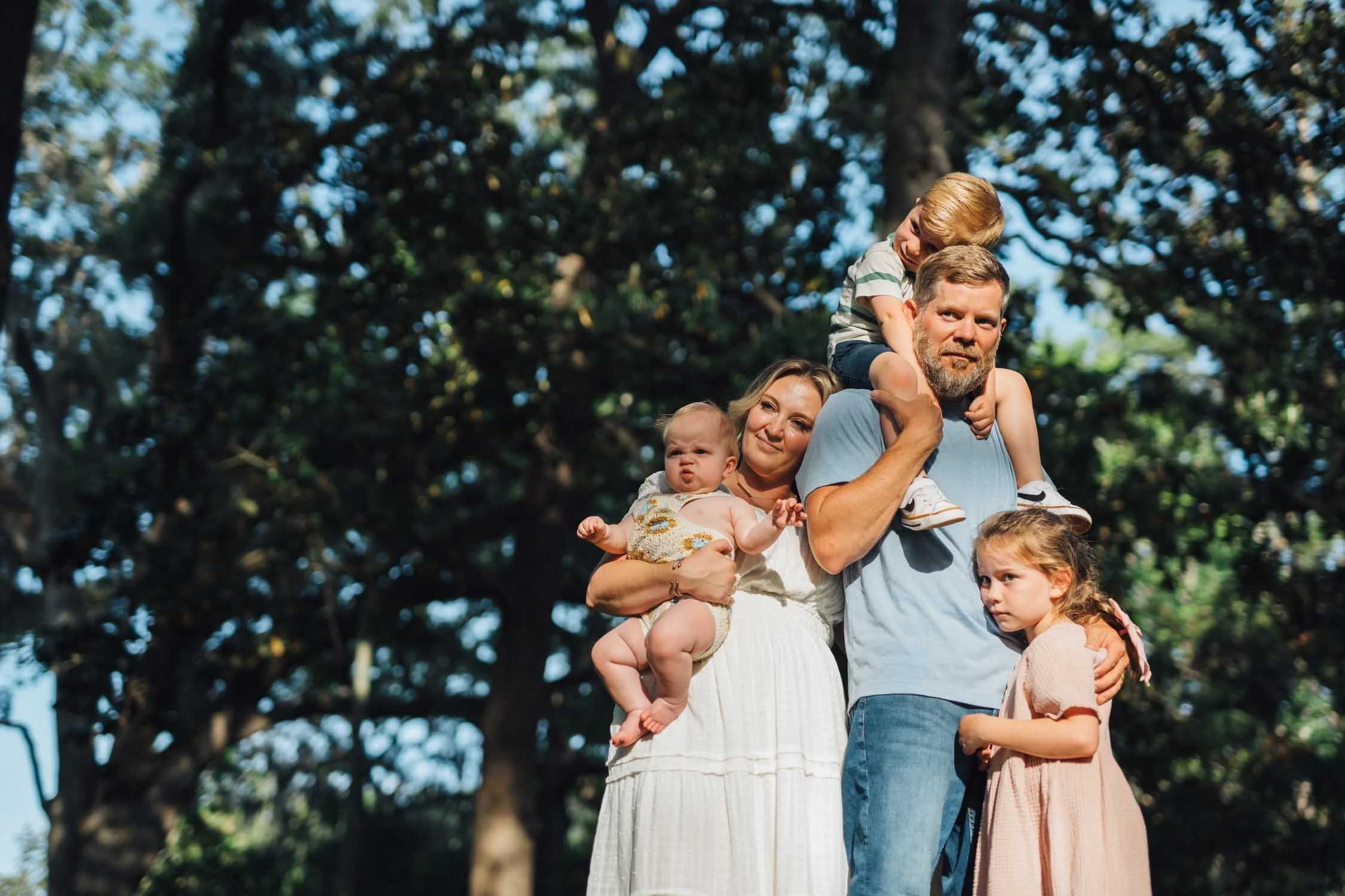 Two parents holding their children on their shoulders in a park during a playful family photography session in Raleigh–Durham.