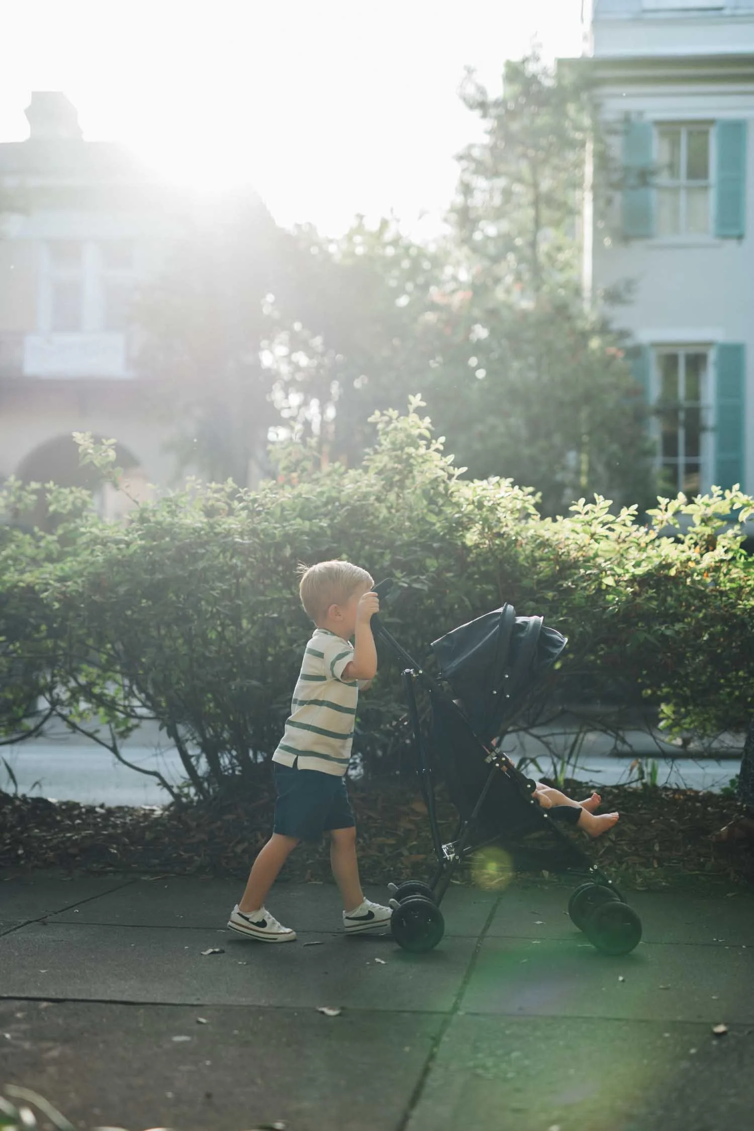 Young child pushing a baby in a stroller along a sidewalk during a Locals family photography session