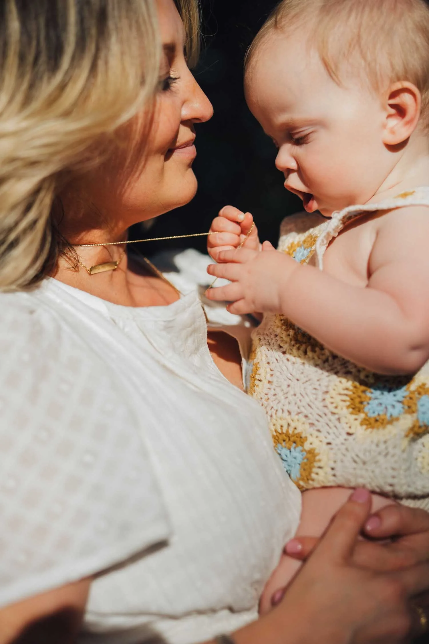 Mother holding her baby as the baby plays with her necklace during a candid lifestyle family photography session in Raleigh, NC.