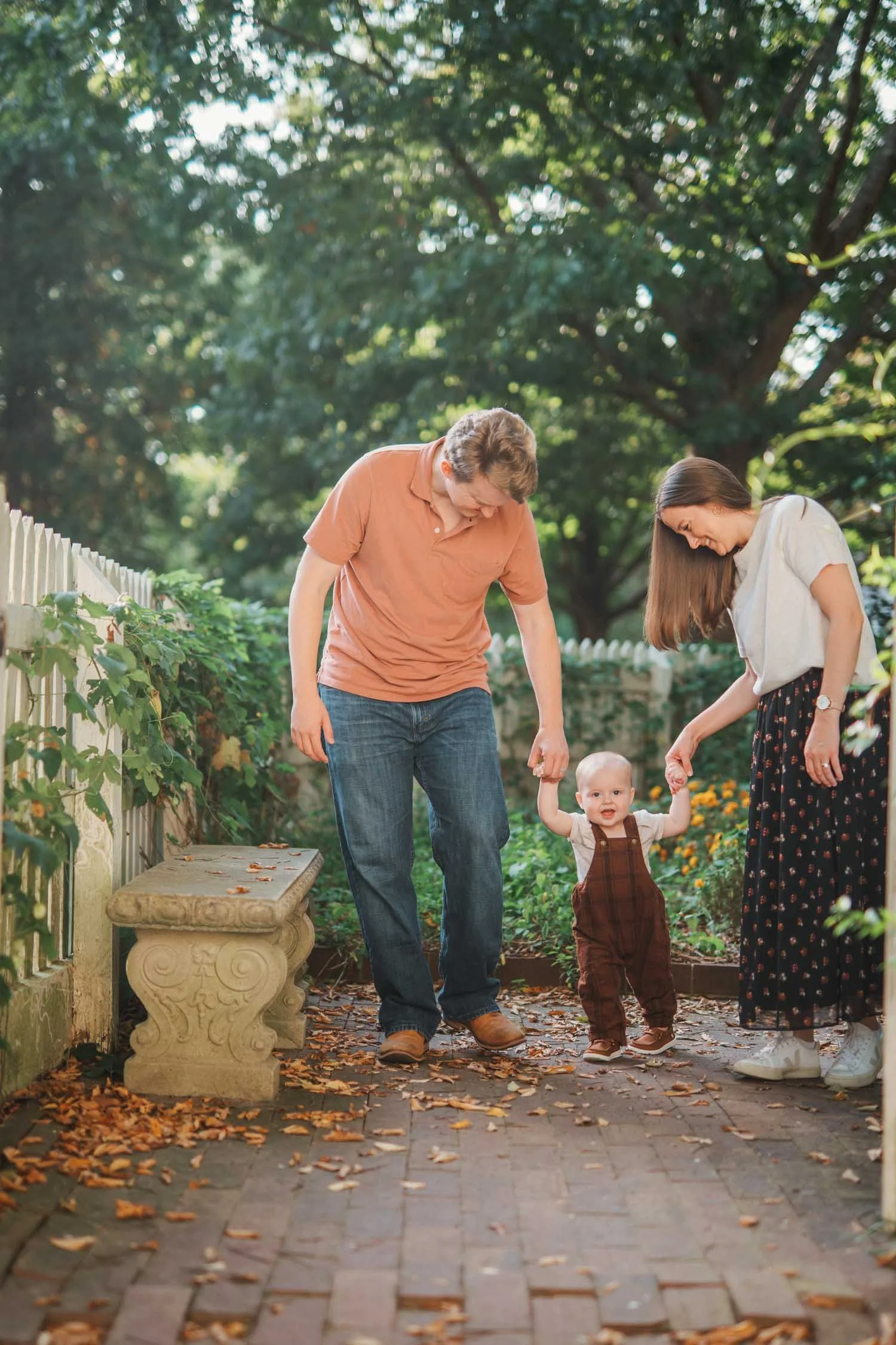Two parents holding their toddler’s hands while walking together outdoors during a family photography session in Raleigh–Durham.
