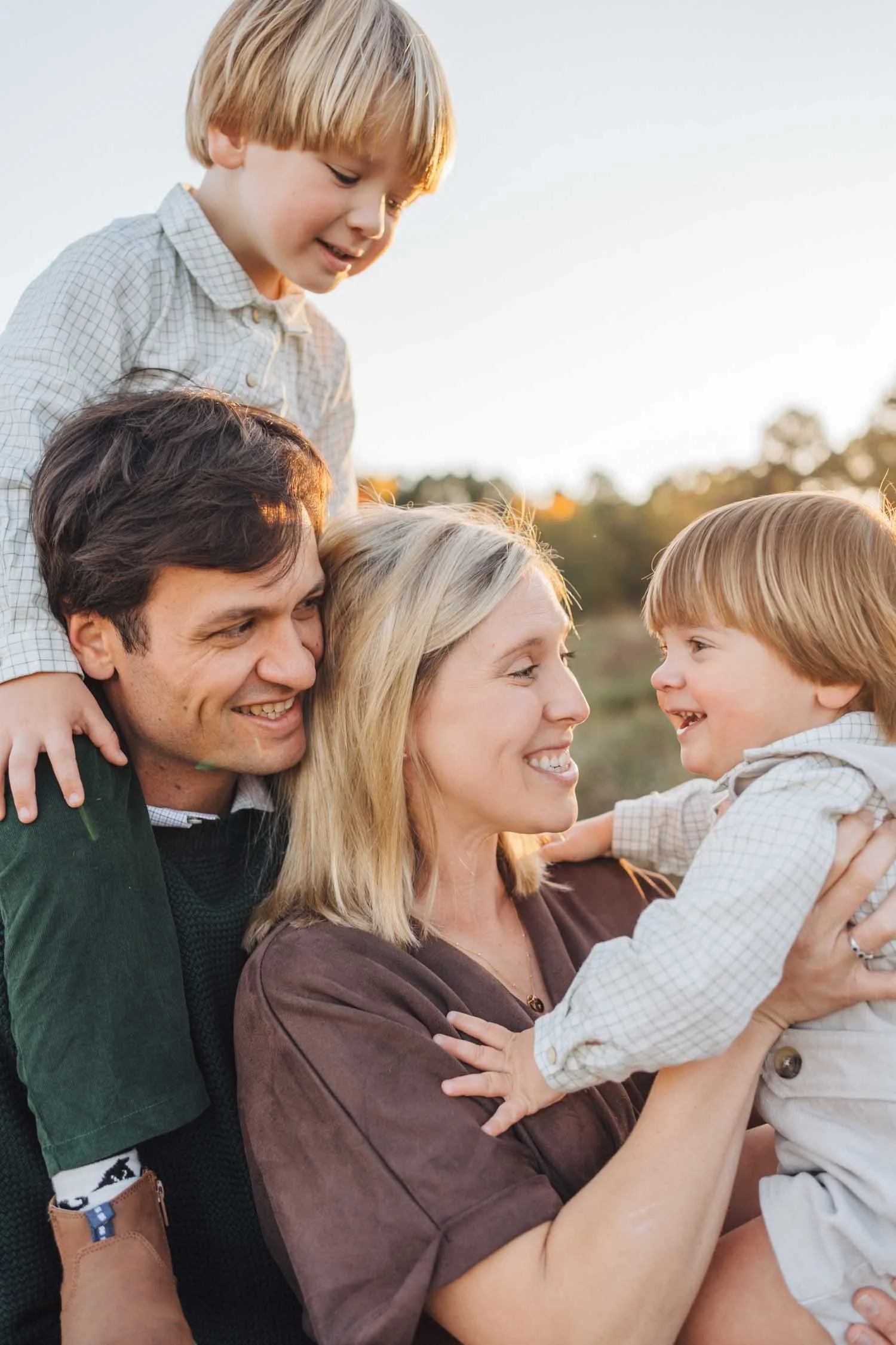 Father carrying a toddler on his shoulders while mother holds another child beside him during a park family photography session in Raleigh, North Carolina.