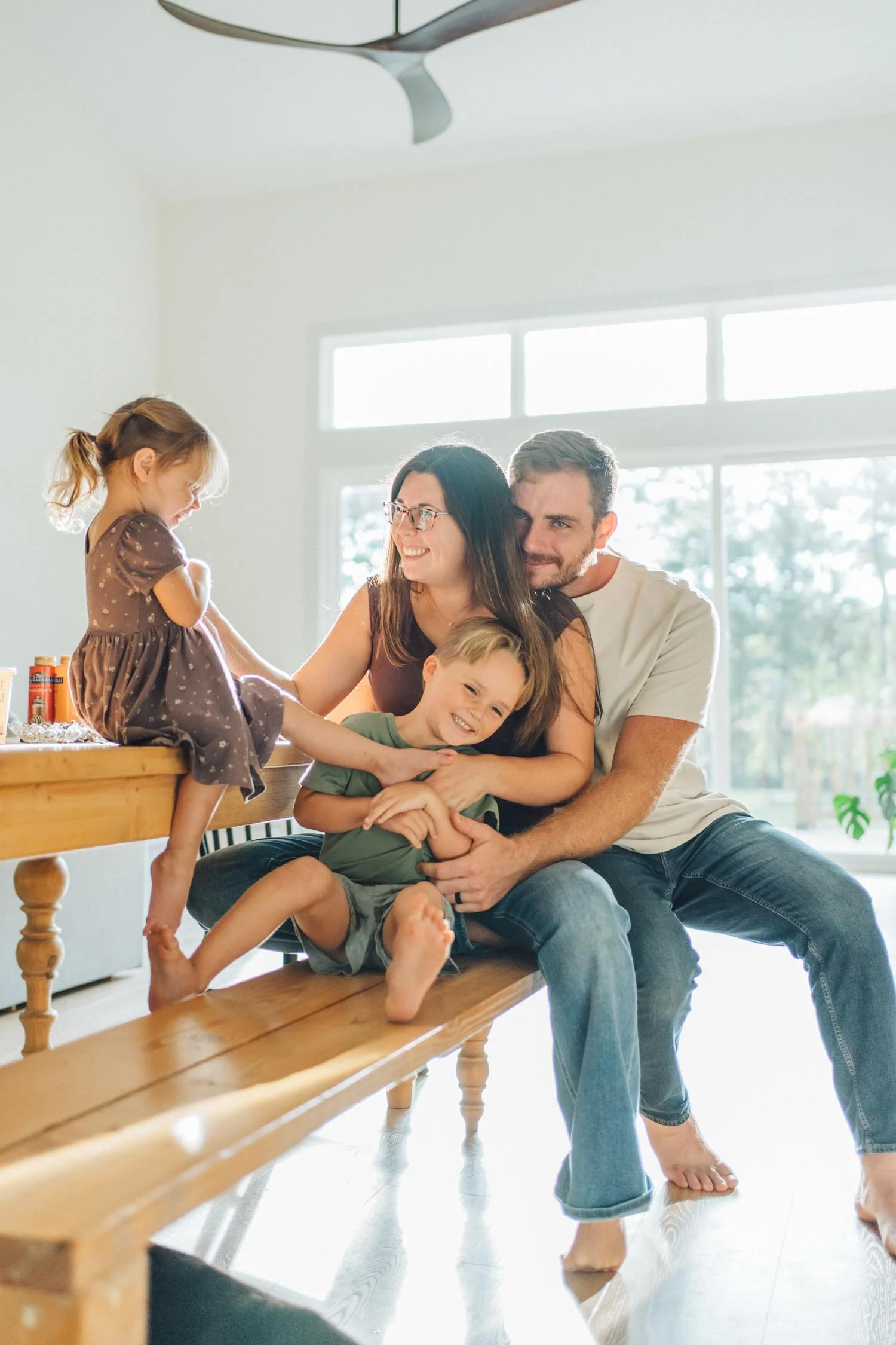 Two parents cuddling with their two daughters on a dining room bench during an in-home family photography session in Raleigh–Durham.