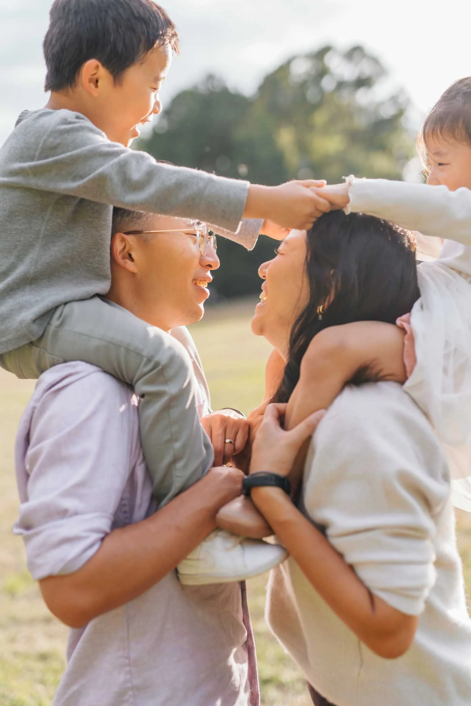 Children holding hands while on their parents' shoulders during a family photography session in Raleigh, NC.