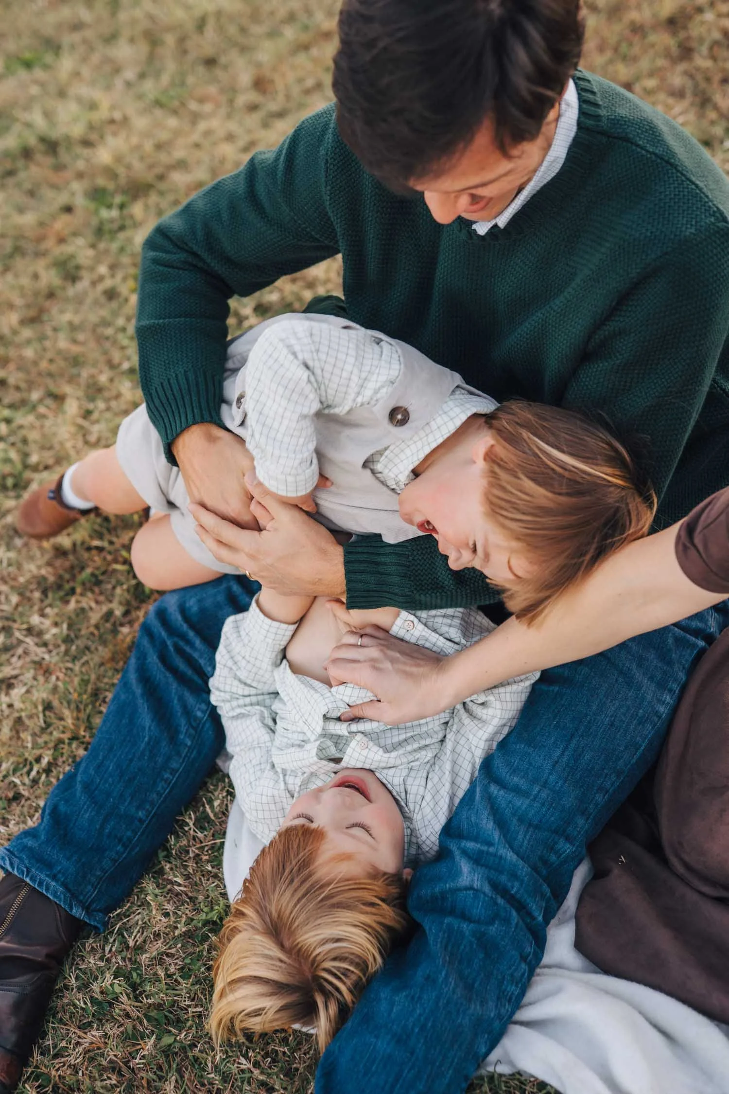Father playing on the ground with two children during a relaxed park family photography session near Chapel Hill, North Carolina.