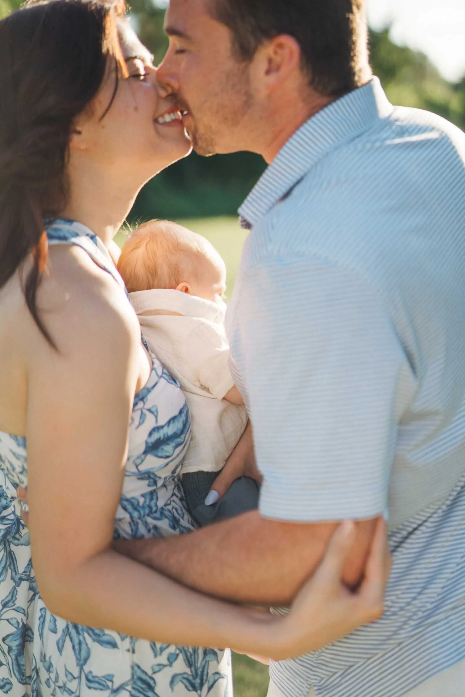Parents kissing while holding their baby during a tender family photography session in Raleigh–Durham.