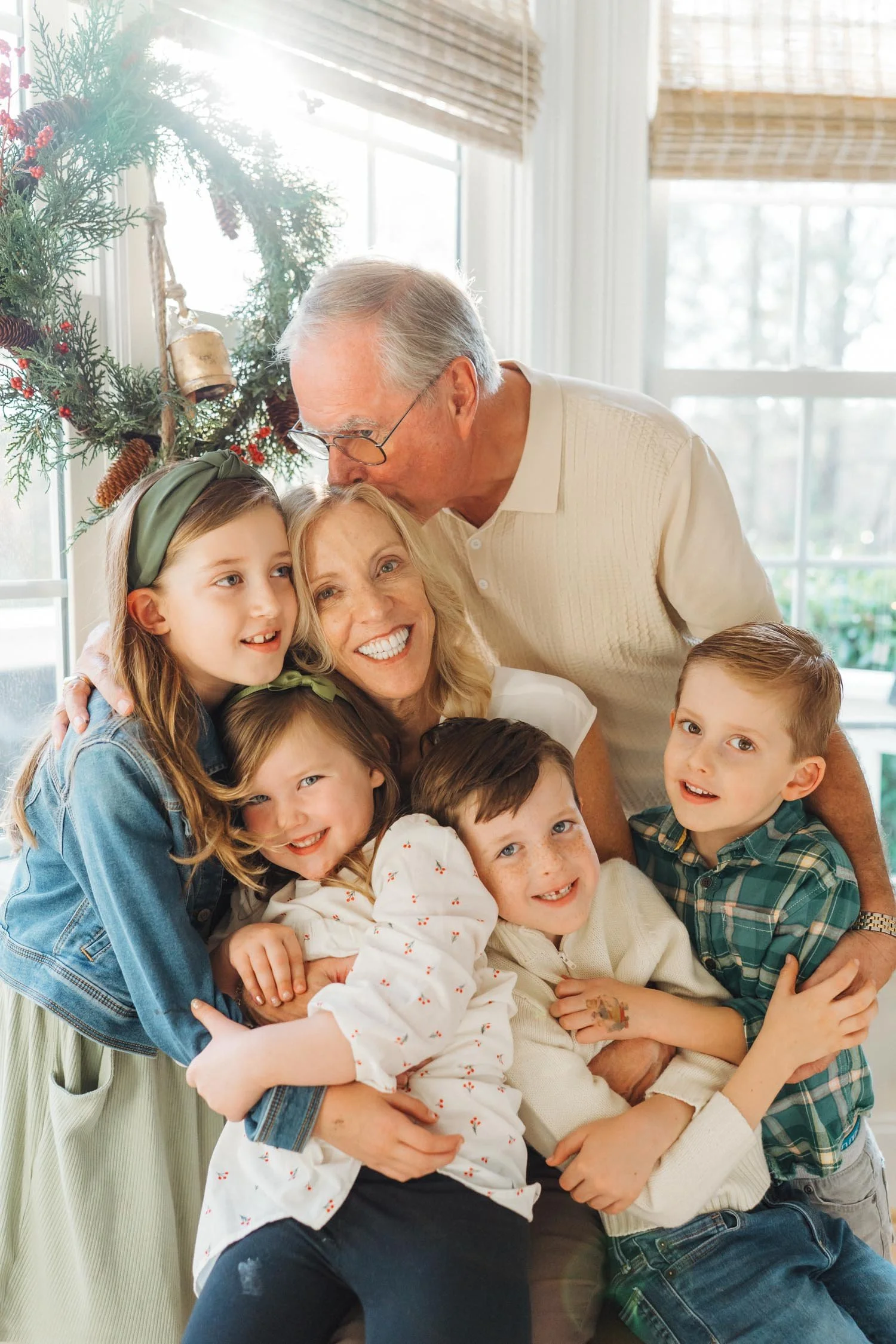 Grandparents sitting in their home surrounded by four grandchildren hugging them during a multi-generational family photography session in Raleigh, North Carolina.
