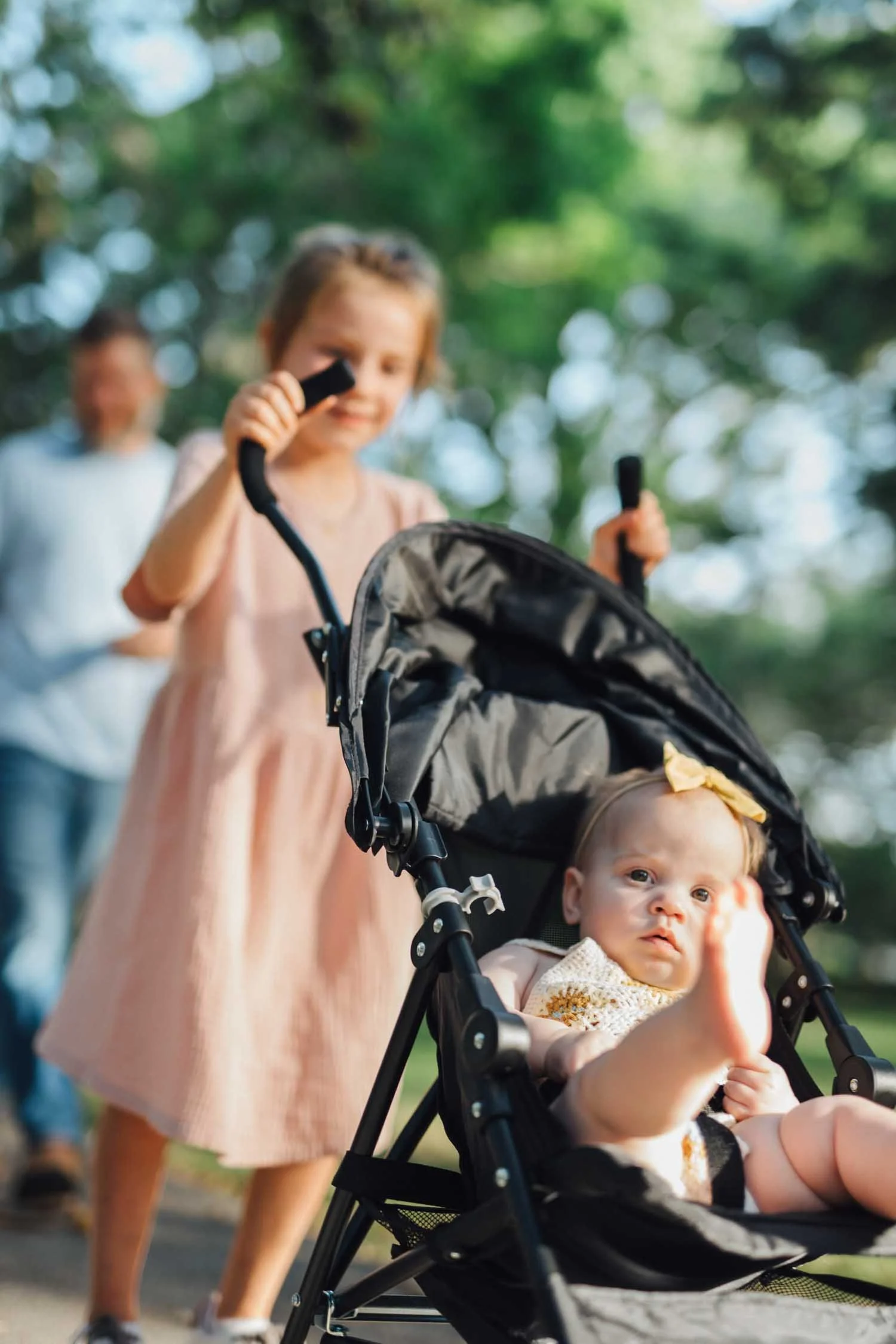 Young girl pushing a baby in a stroller along a park path during a Locals family photography session in Raleigh–Durham.