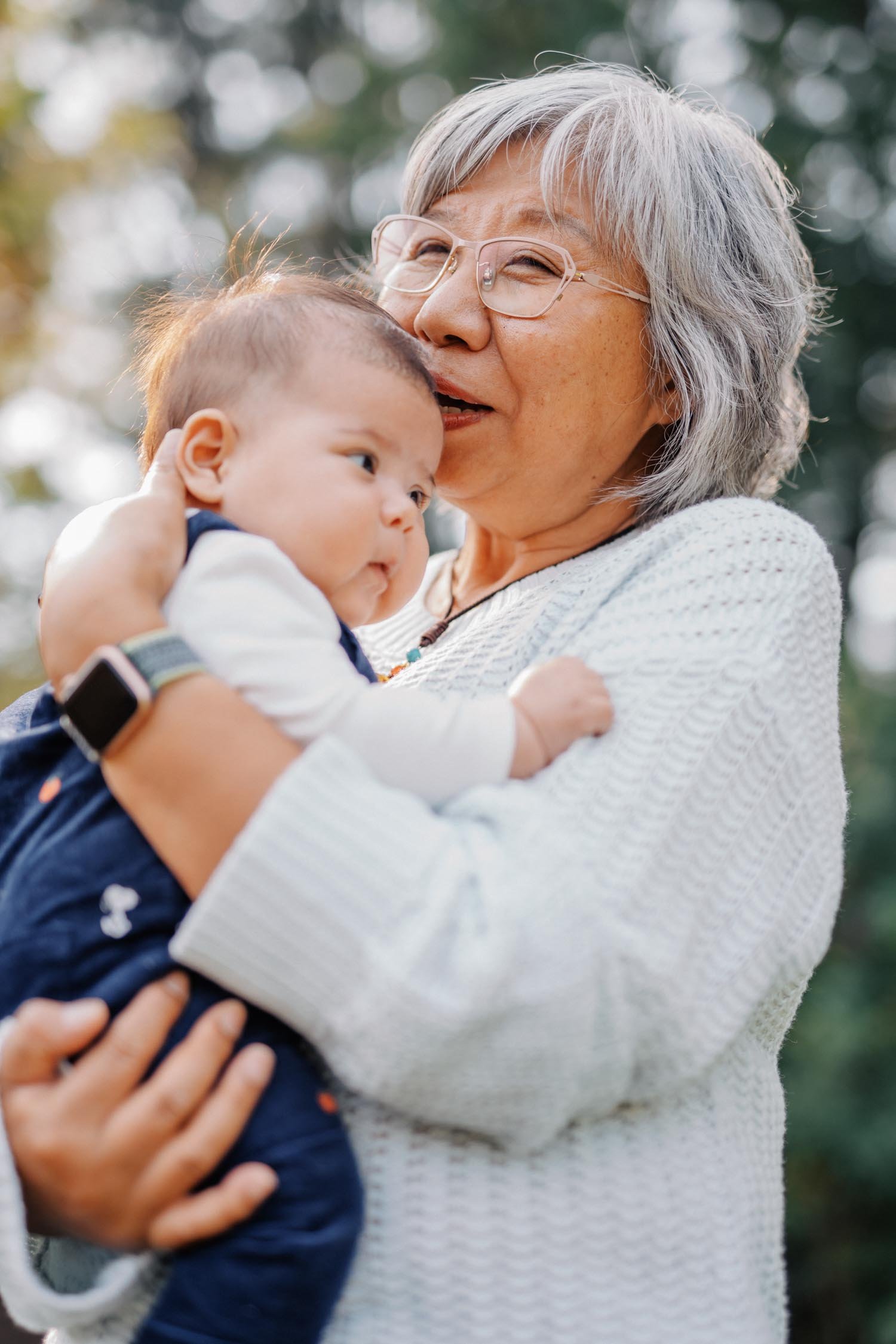 Grandmother holding and kissing a baby in the backyard during a multi-generational family photography session in Raleigh, NC.