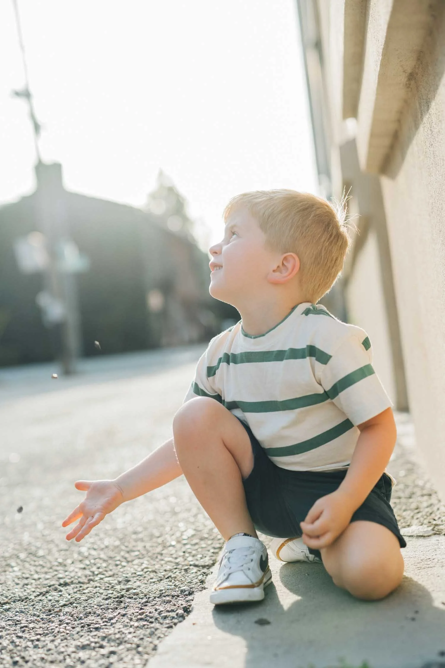 Young boy kneeling and looking up along a sidewalk in a walkable downtown area during a lifestyle family photography session in the Raleigh–Durham area.