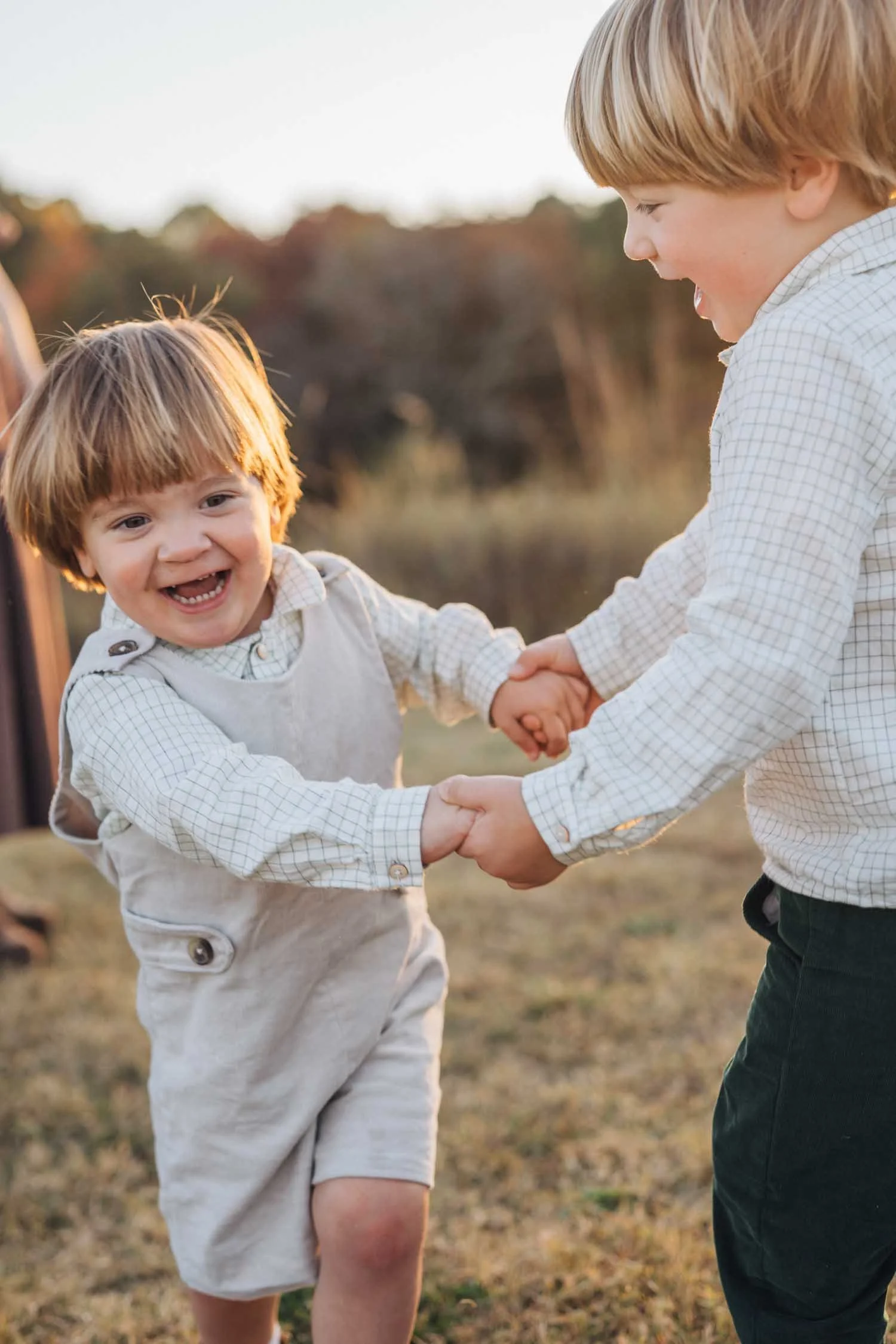 Two children holding hands and playing together in a park at golden hour during a park family photography session in Raleigh, NC.