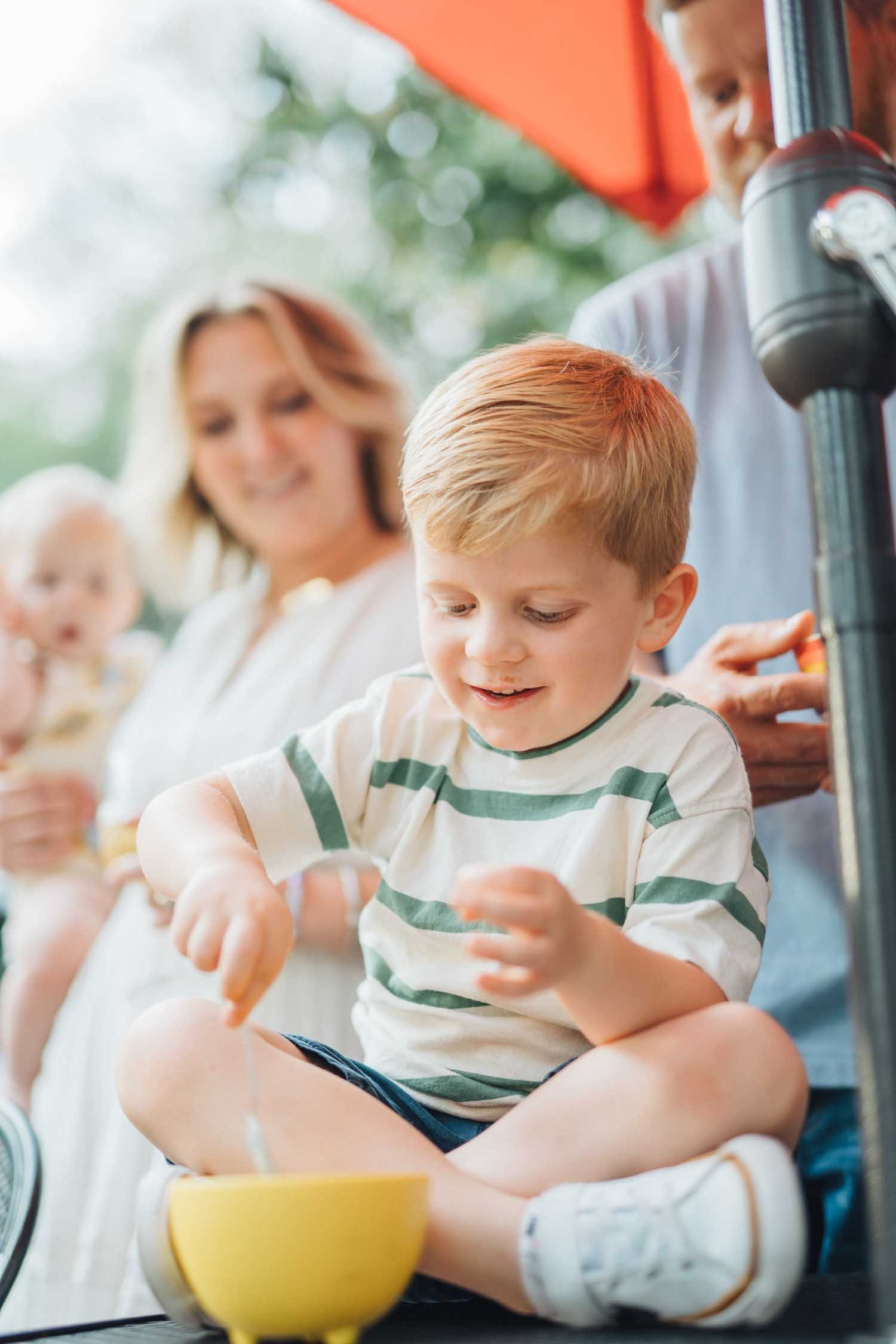 Young boy eating a snack from a bowl outdoors with his parents during a natural family photography session in Raleigh–Durham.